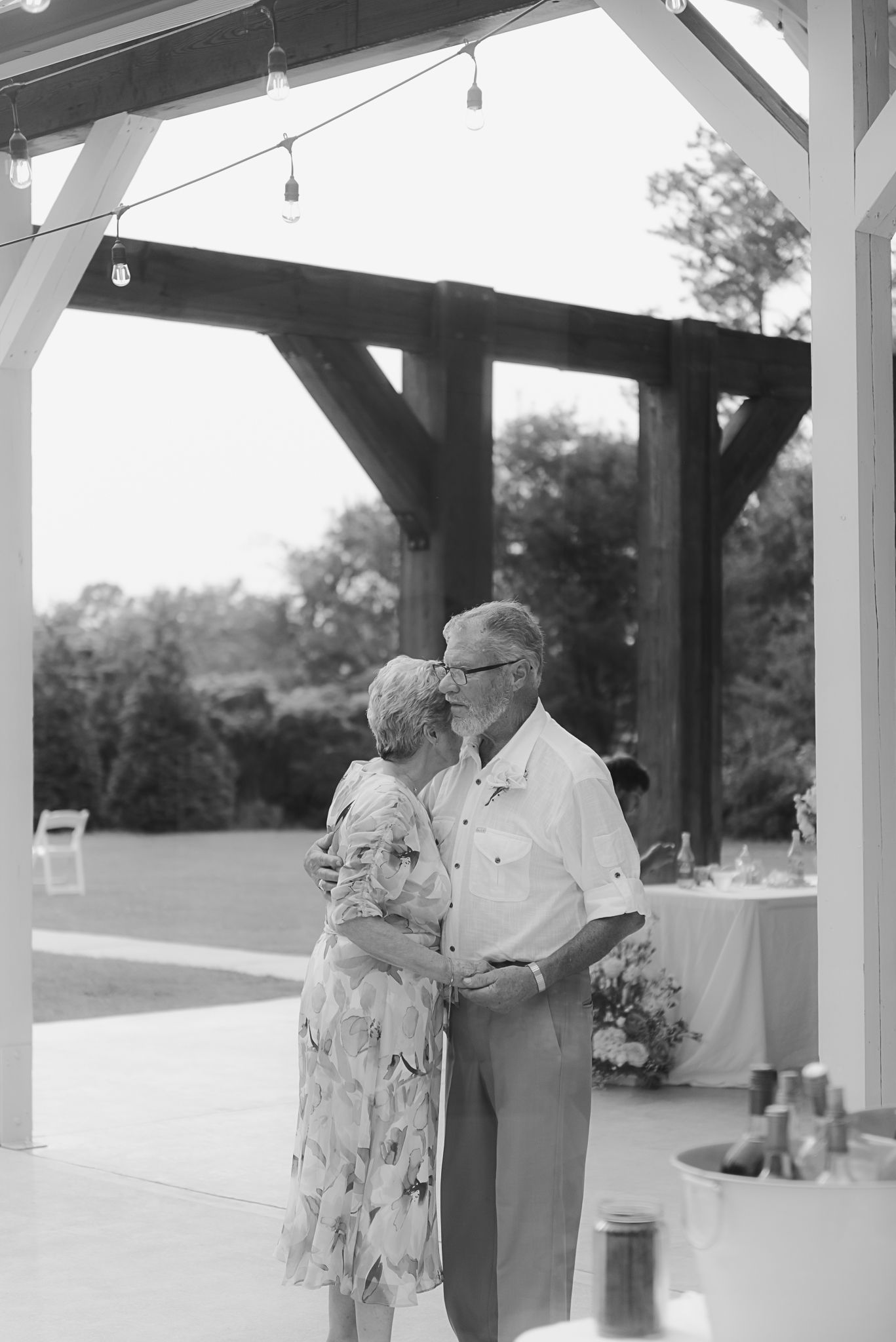 Black and white photo of couple sharing a tender moment under outdoor pavilion.