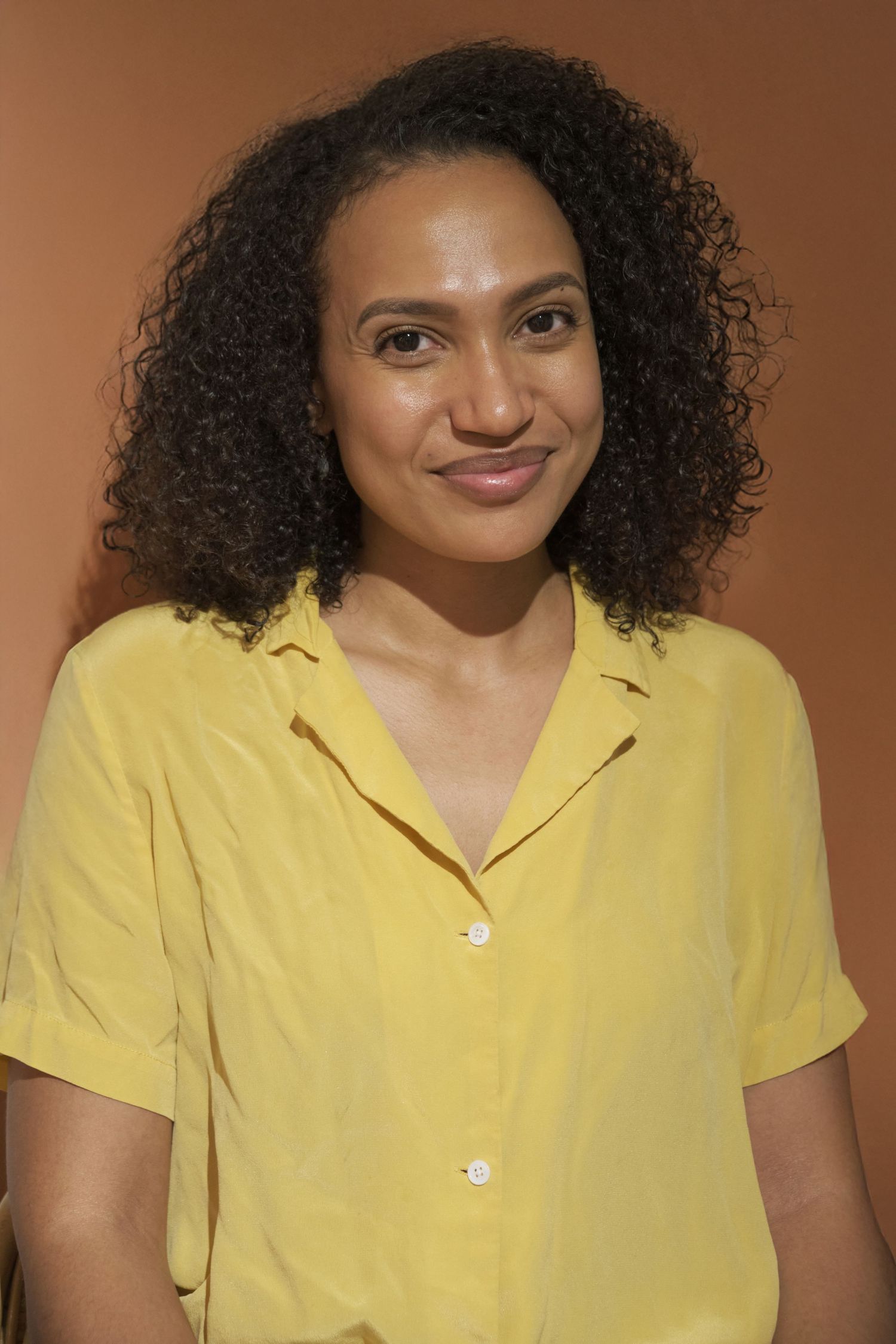 Person wearing a bright yellow collared shirt smiles against a brown background in a series of portrait photos.