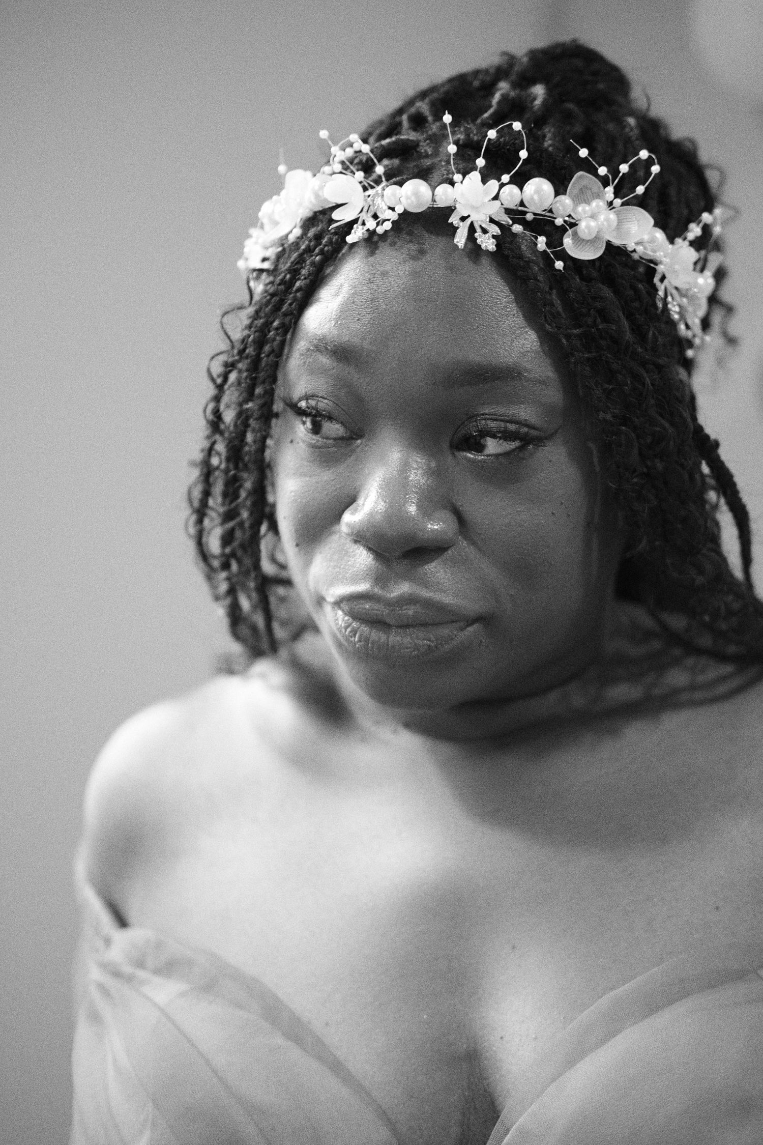 A black and white portrait of someone wearing a delicate floral headpiece and off-shoulder dress.