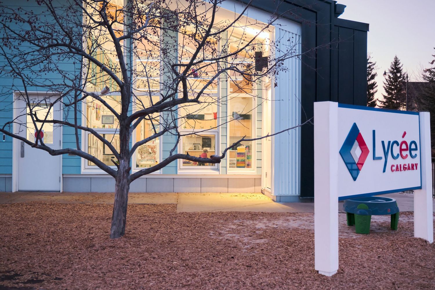 Modern building exterior with bare trees and Lycee signage against a bright sky at dusk.