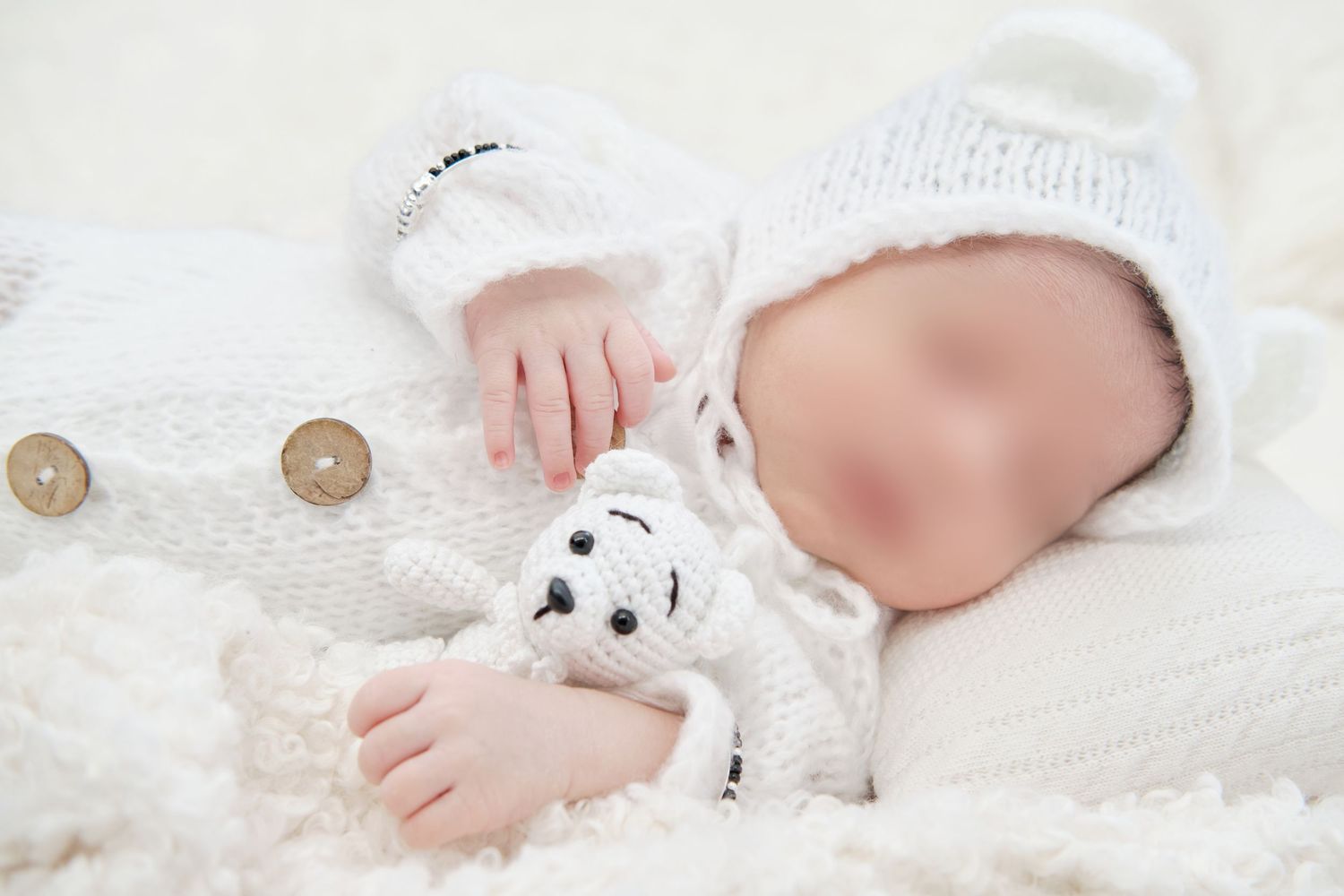 A newborn baby's feet and hands rest on soft white blankets with a small stuffed animal toy nearby.