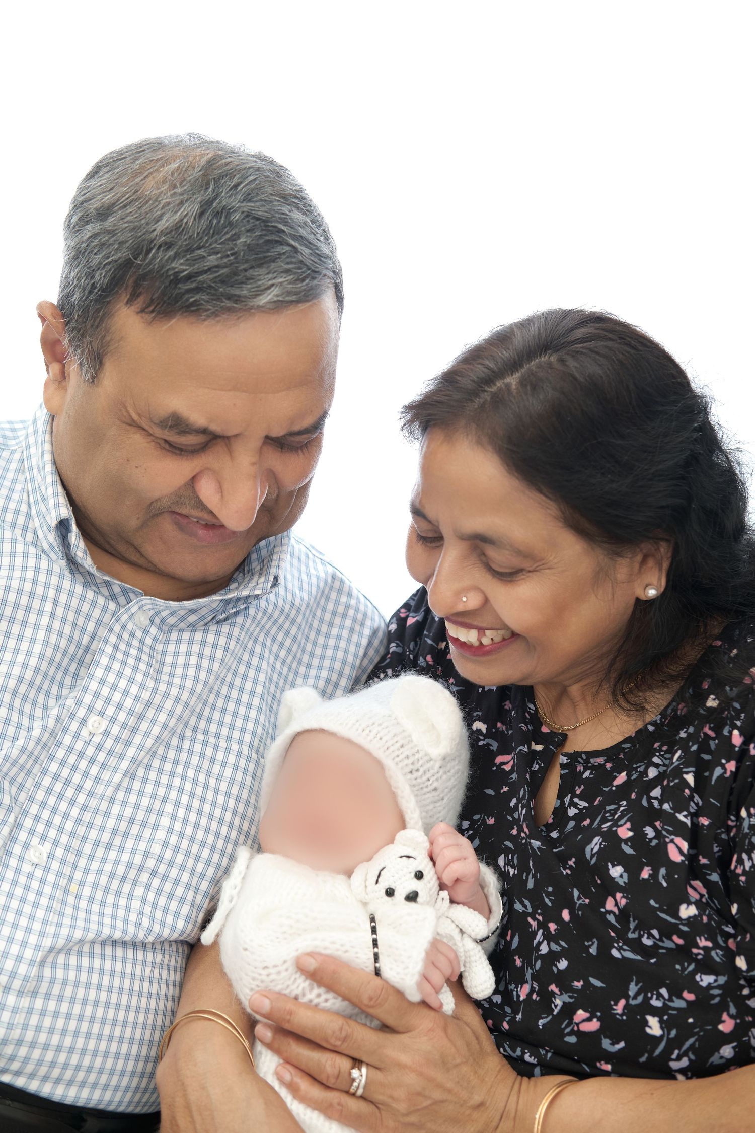 A couple smiles lovingly while holding and admiring a small white stuffed animal toy together.
