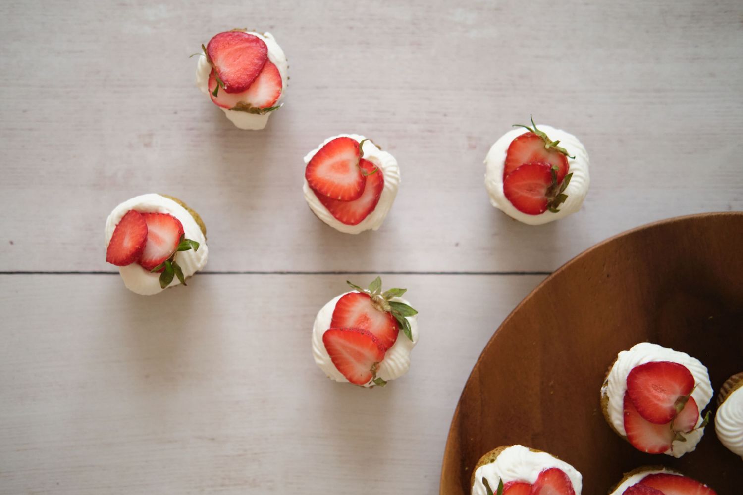 Mini pistachio cupcake topped with orange blossom water whipped cream and fresh strawberries arranged in a decorative pattern.