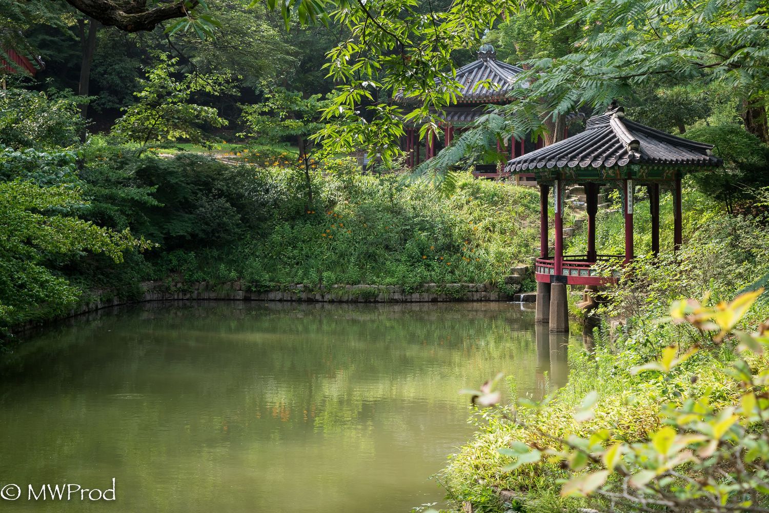 Serene Korean garden landscape with traditional pavilions and a tranquil pond surrounded by lush greenery.