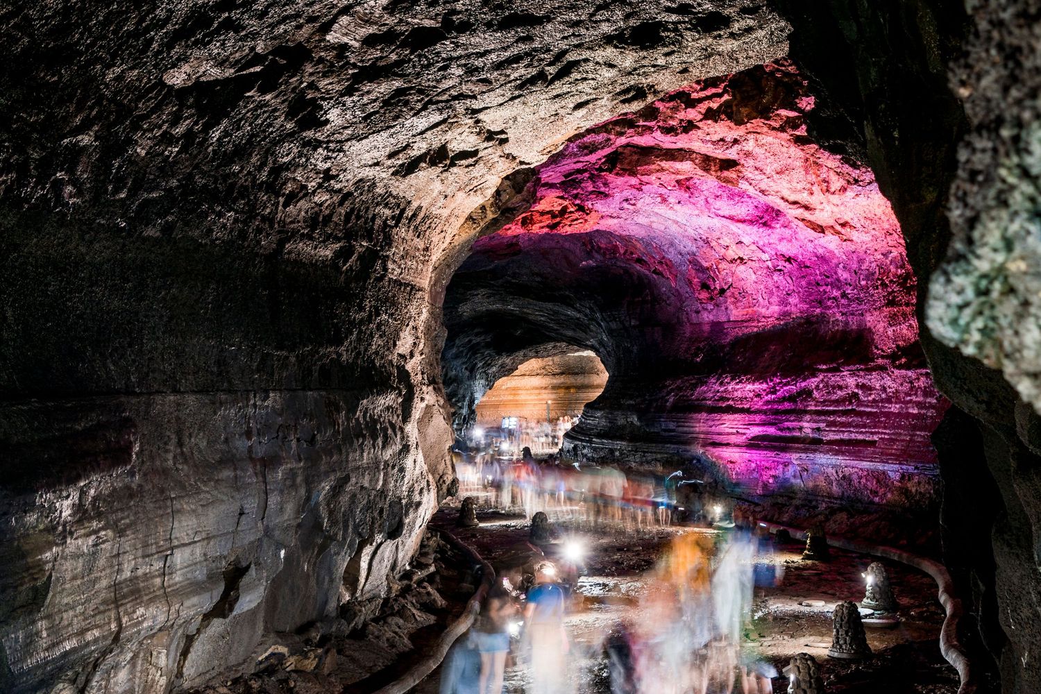 Illuminated cave interior with colorful purple lighting and rock formations.