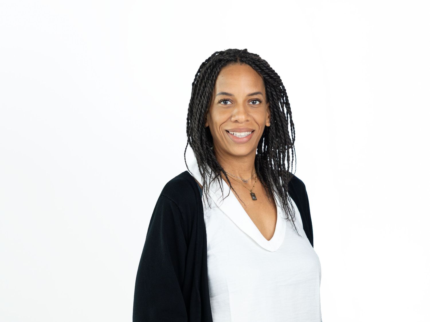 Smiling woman with long braided hair wearing a black cardigan over a white top with a pendant necklace.