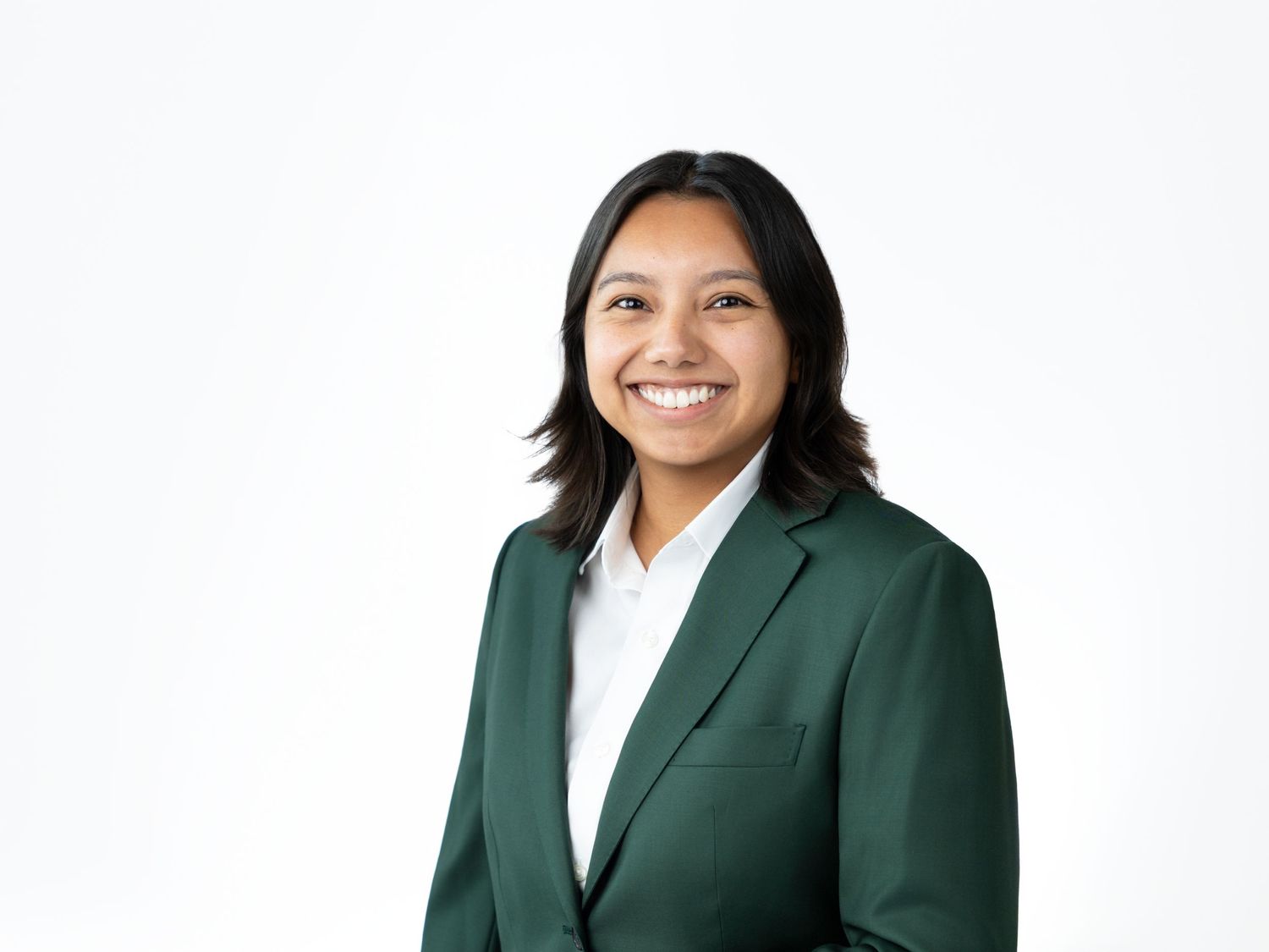 Smiling woman with shoulder-length dark hair wearing a forest green blazer over a white collared shirt against a white background.