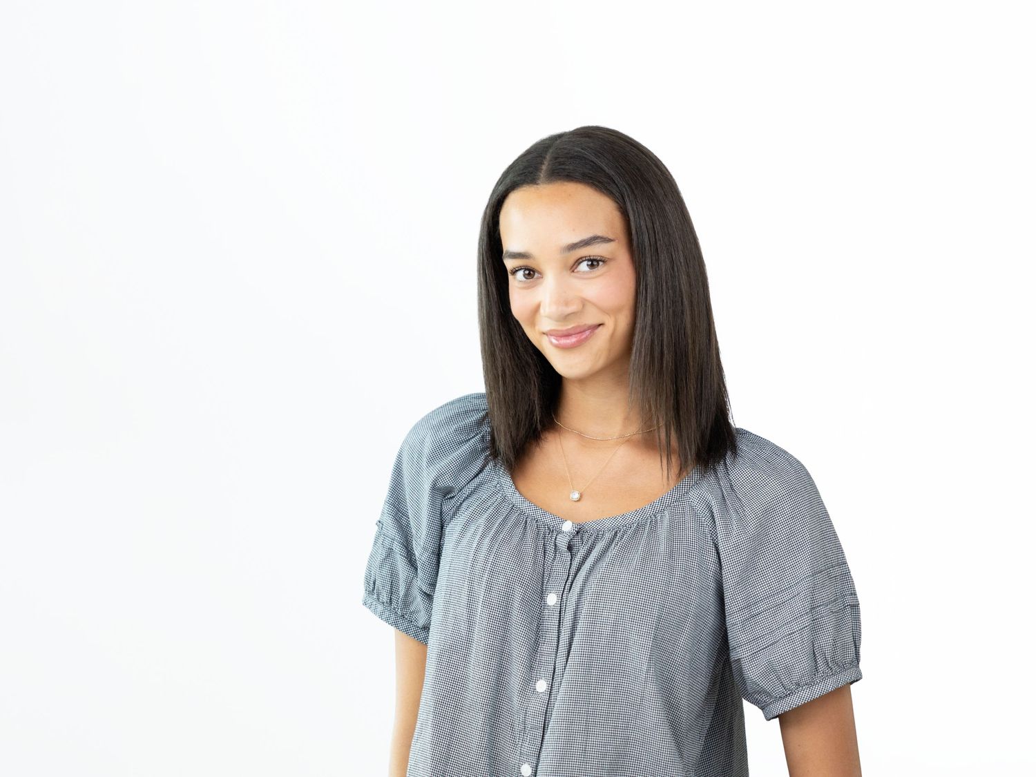 Young woman with straight dark shoulder-length hair smiling softly in a gray short-sleeved button-up top.