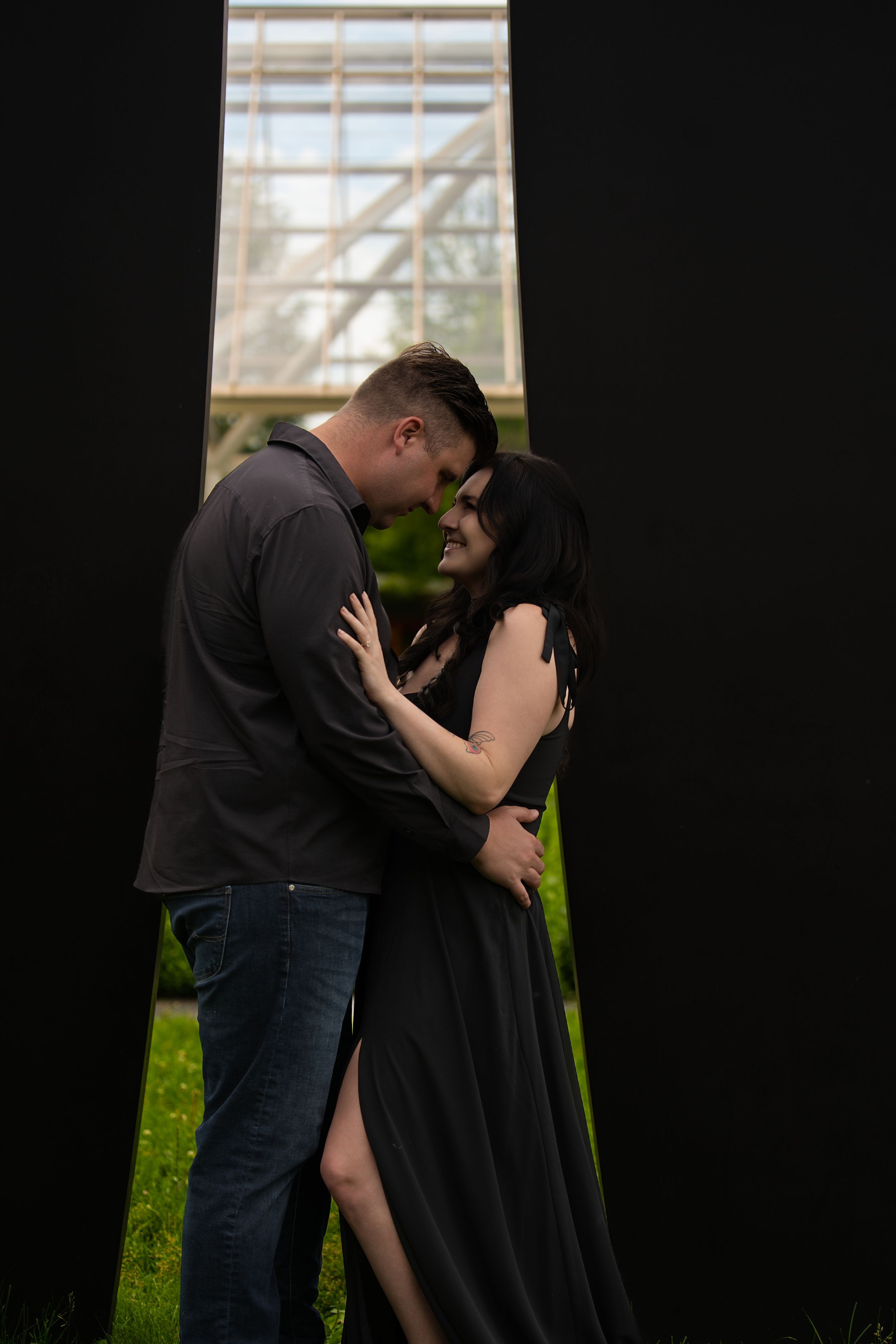 A couple embracing in a dark doorway with a glass conservatory glowing behind them
