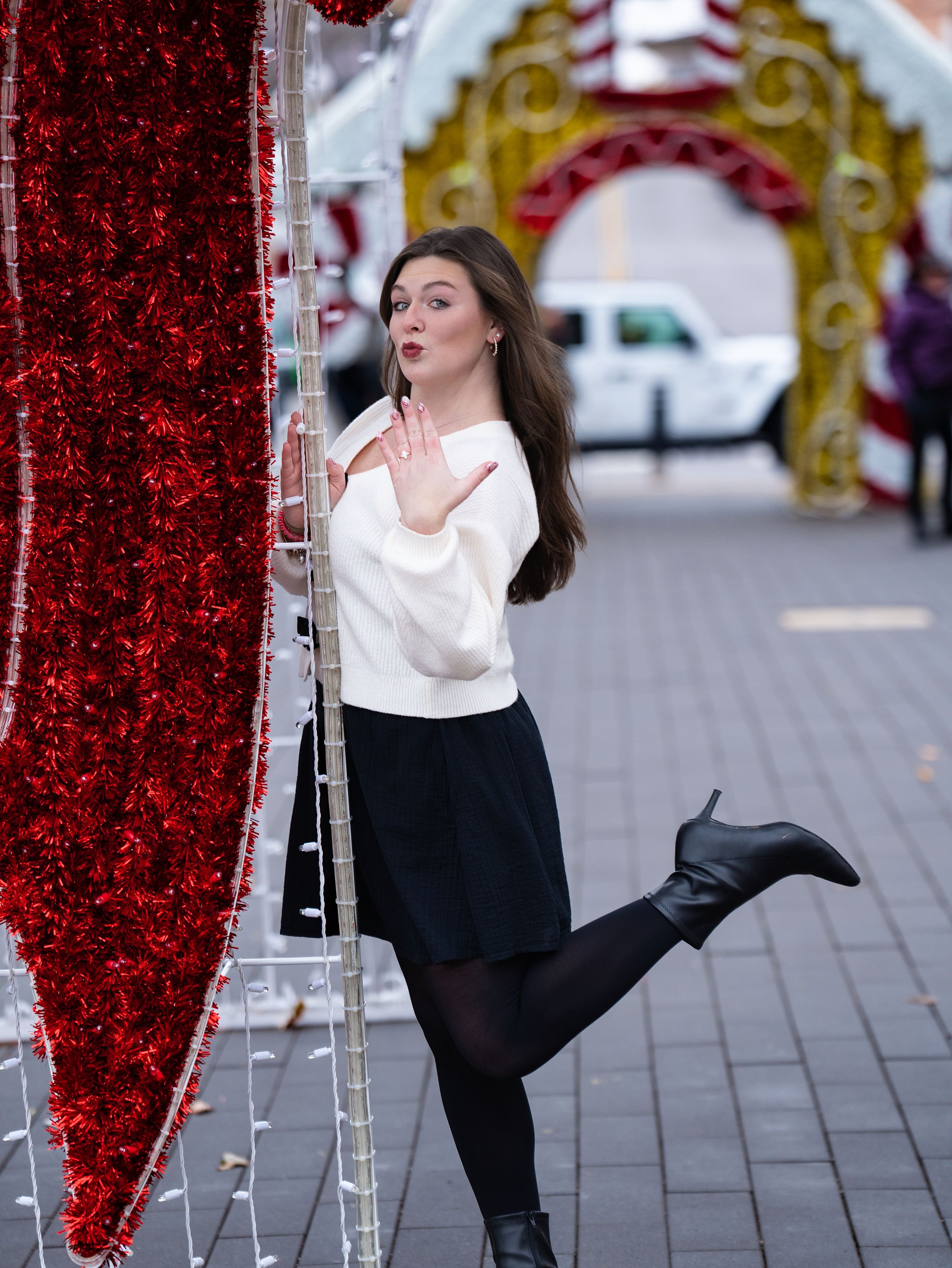 A woman shows off her engagement ring with a playful pose among festive holiday decorations
