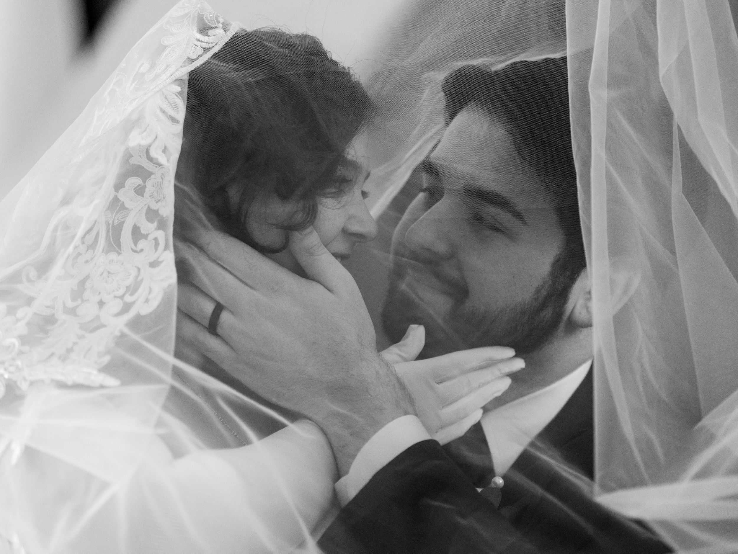 A bride and groom share a tender moment under her lace veil in black and white