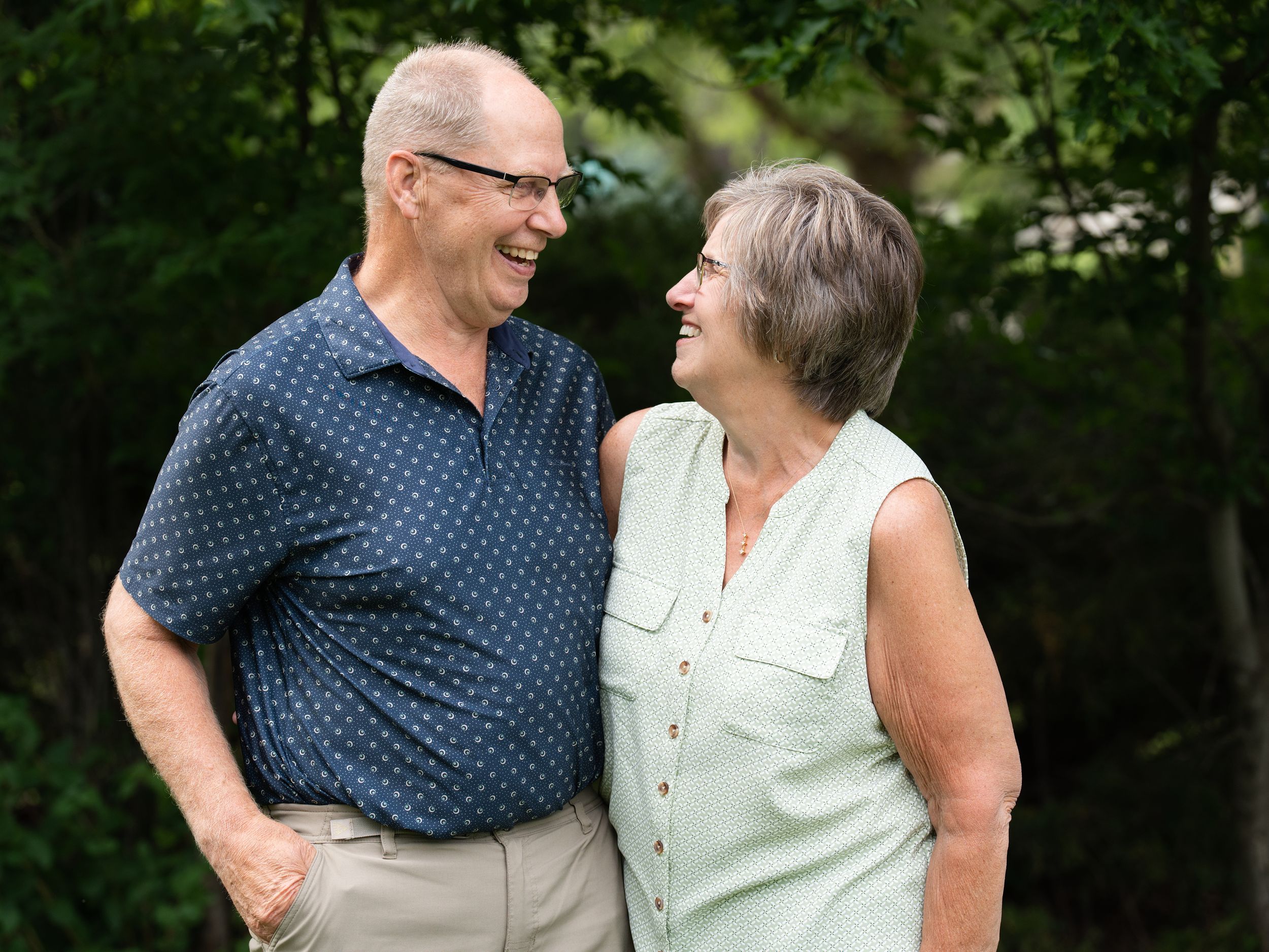 An older couple laughing and gazing at each other in a leafy garden