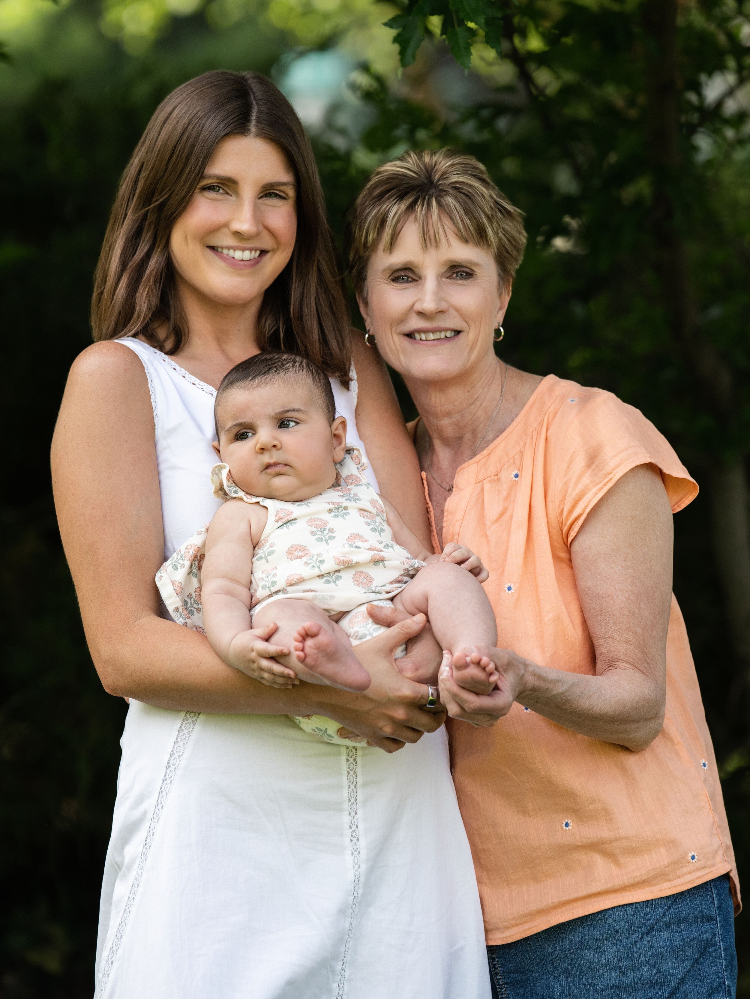 A woman holding a baby beside an older woman in a leafy garden