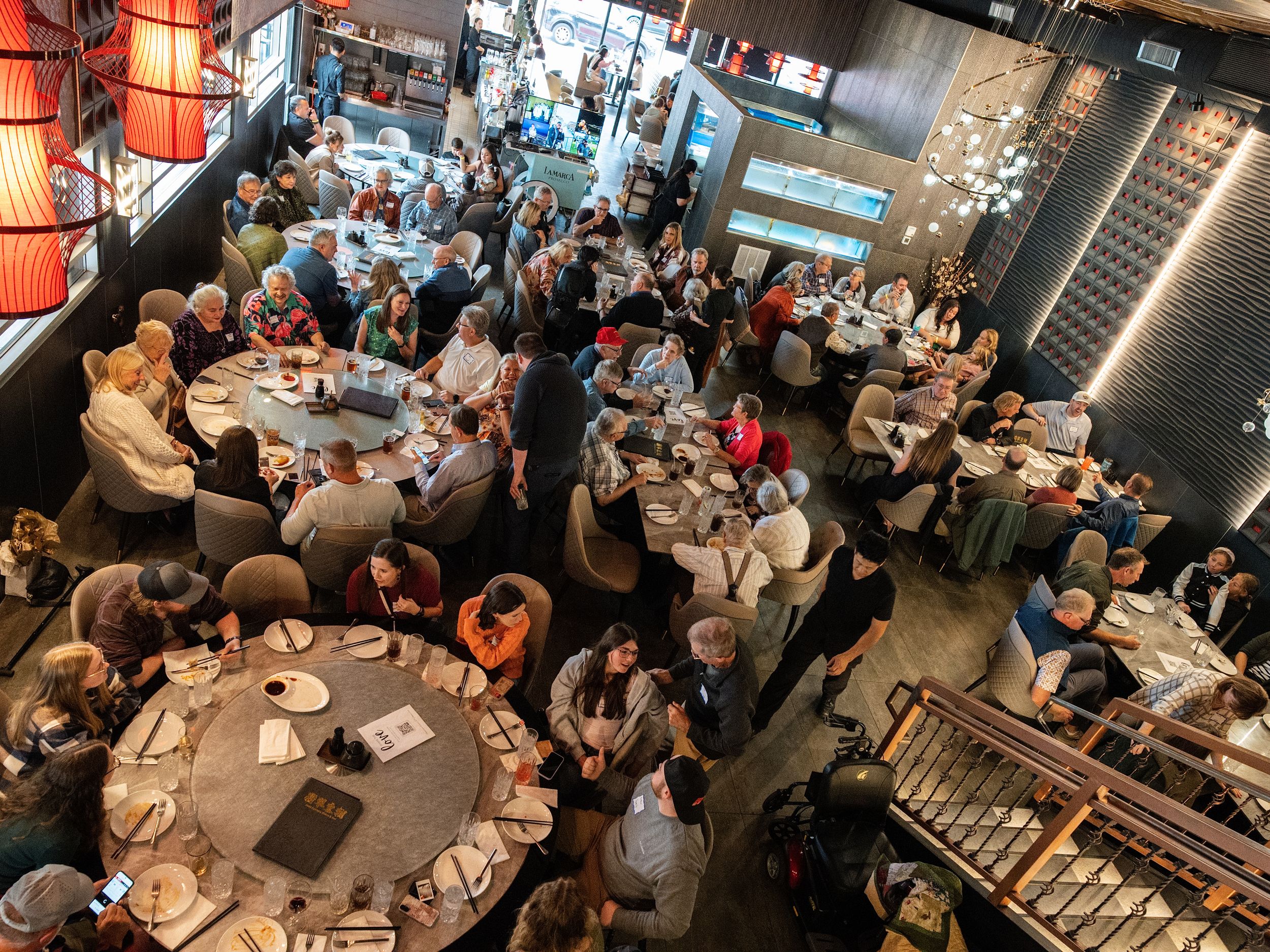 An overhead view of guests seated at round tables during a busy restaurant event