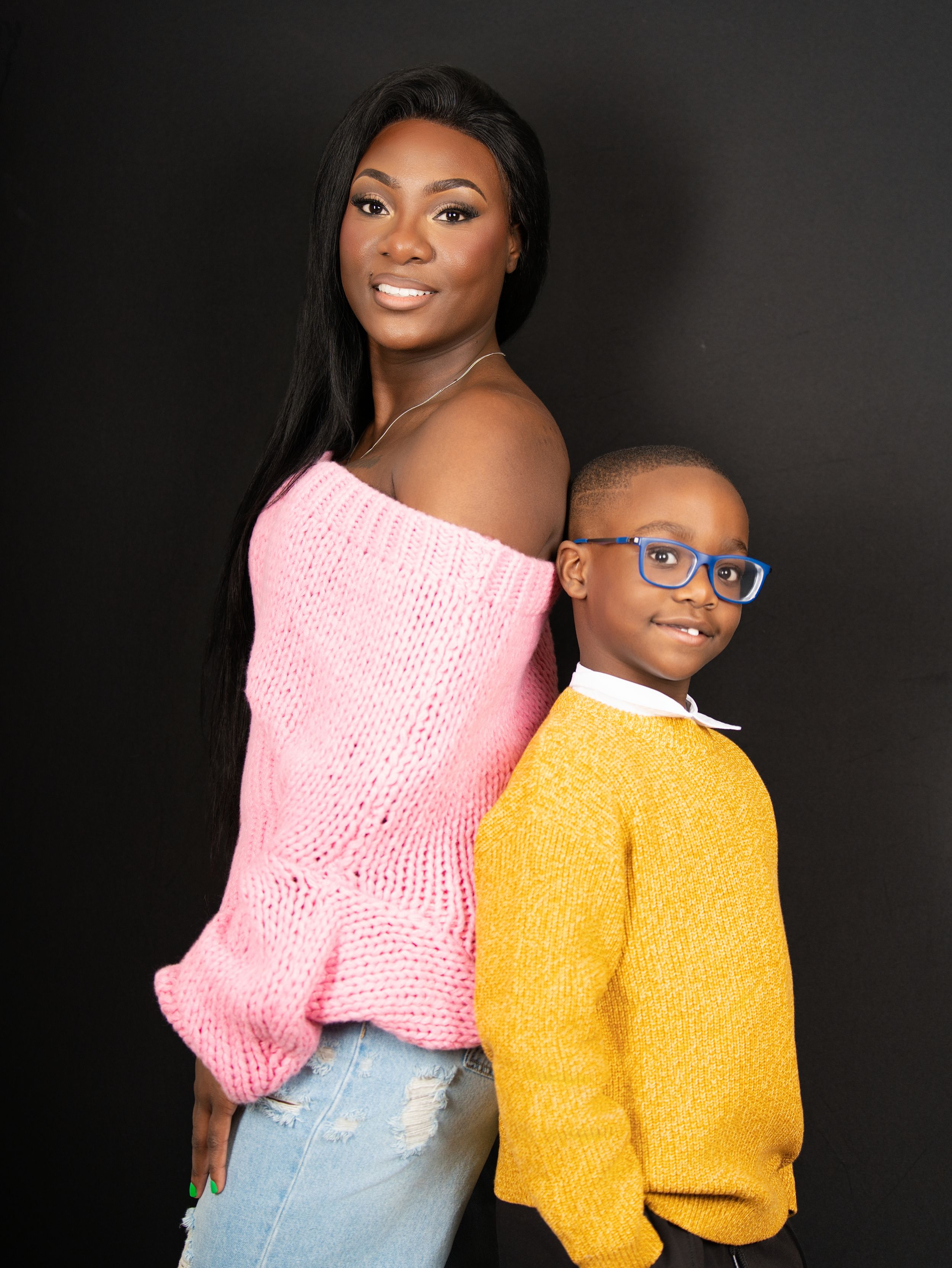 A woman and a young boy in a yellow sweater posing against a dark studio backdrop