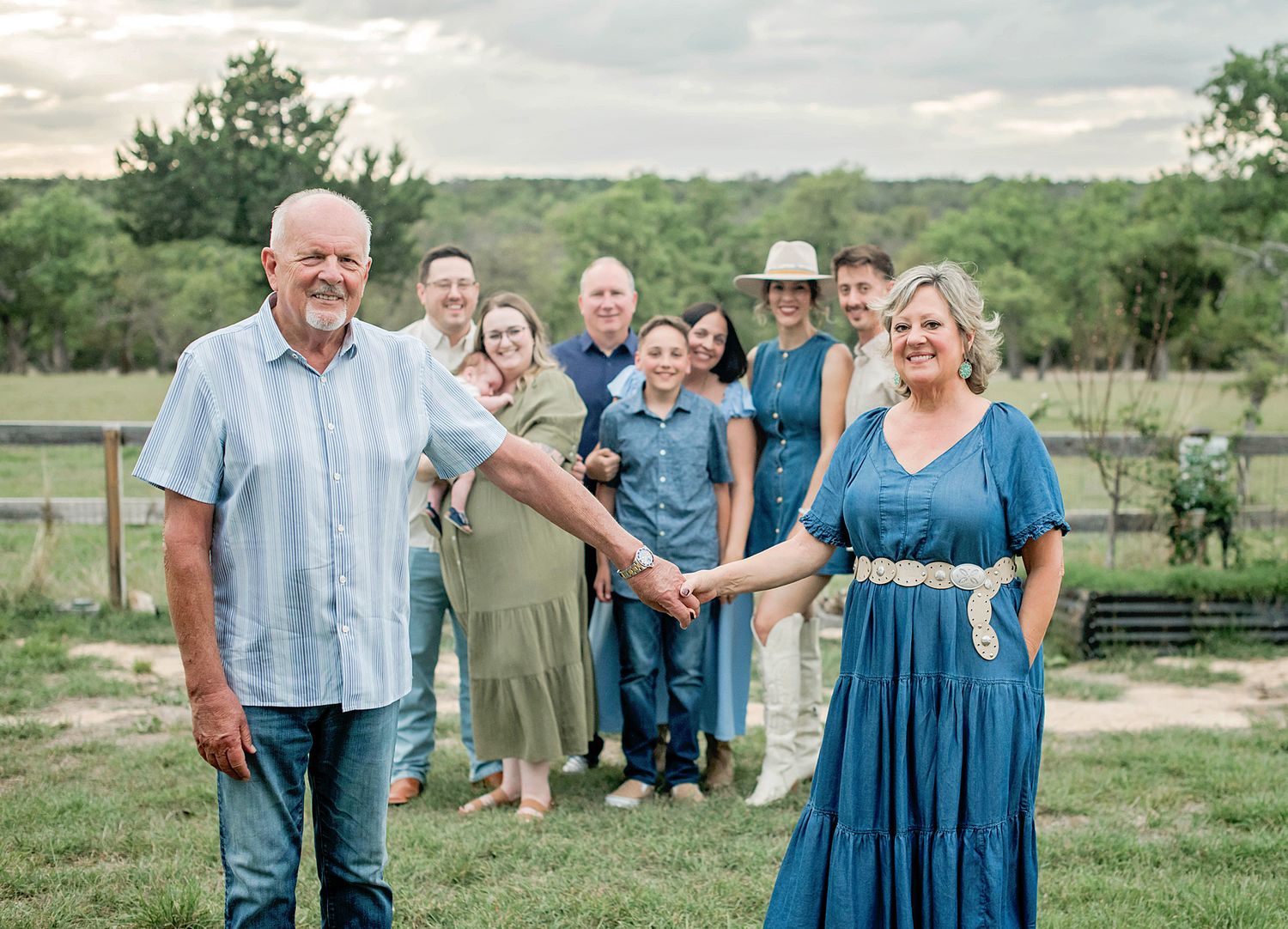 A joyful family group poses outdoors on a green farm, with an older couple holding hands in the foreground.