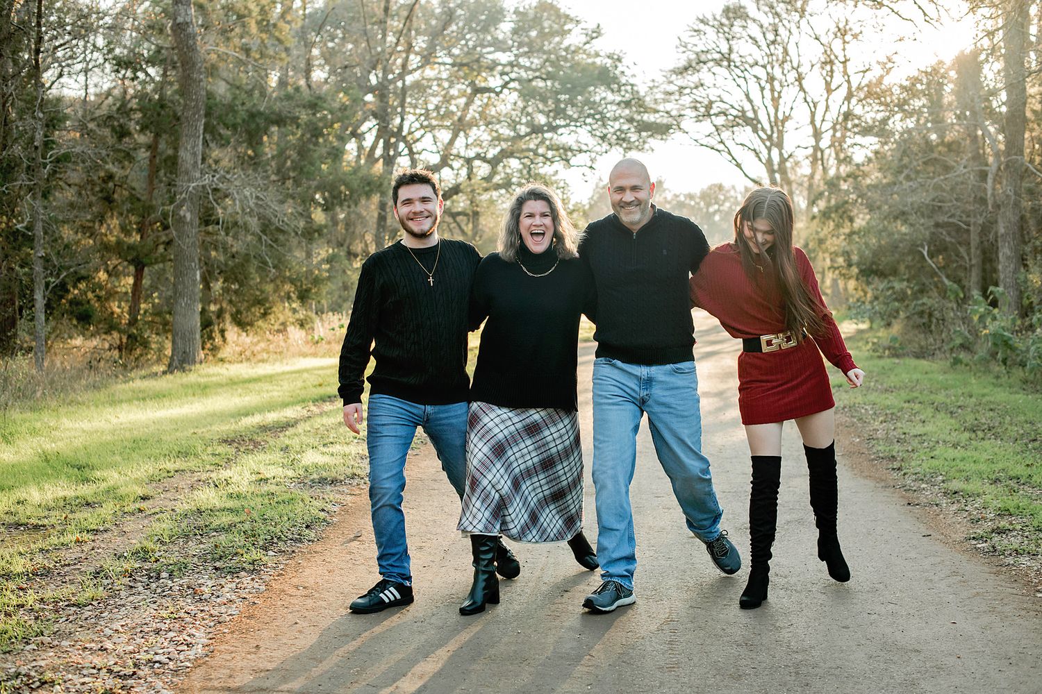 Happy family of four posing on a scenic dirt path surrounded by trees during an outdoor photo session.