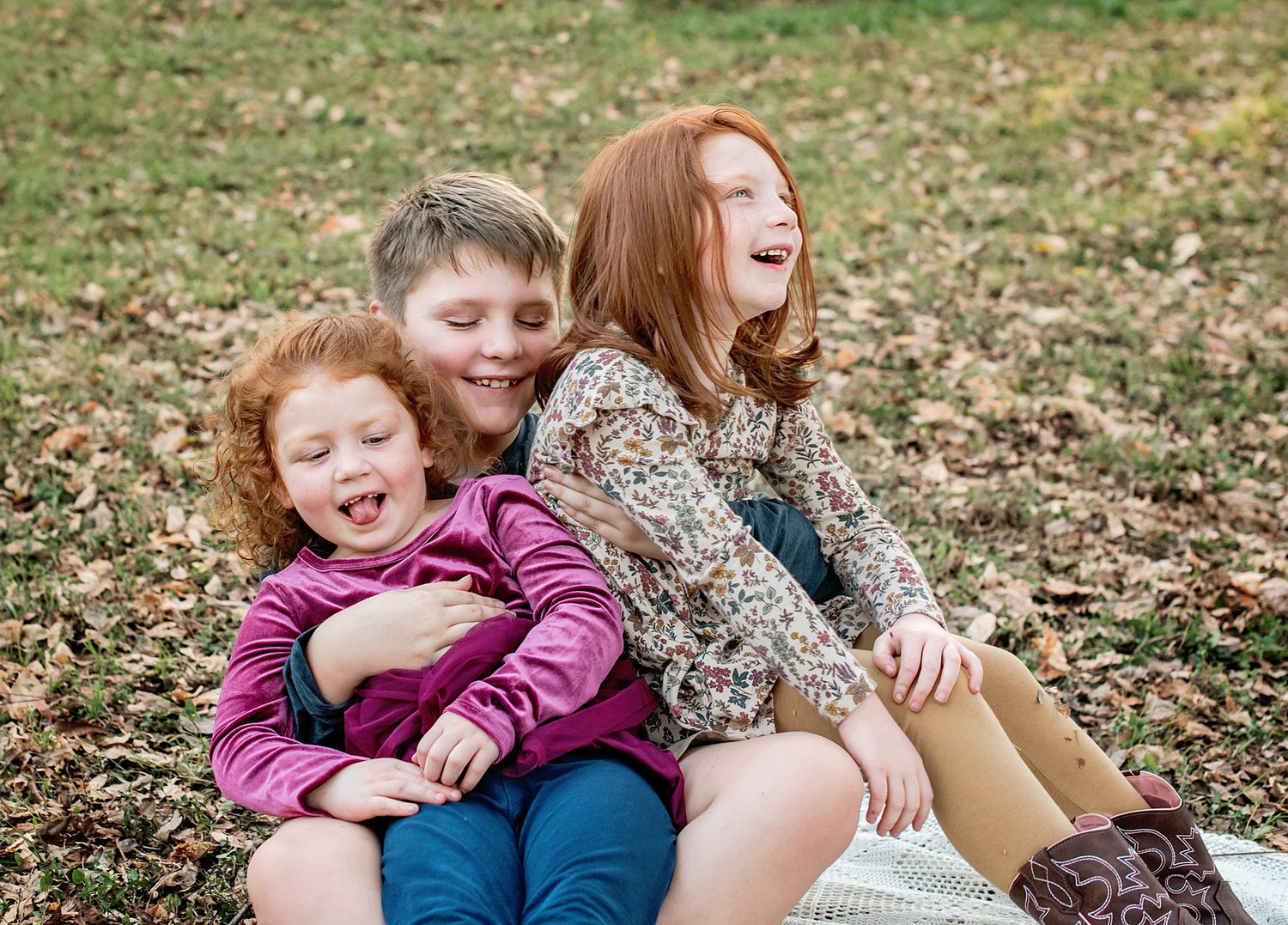 Playful candid moments of siblings laughing and embracing on grass during a photo shoot.
