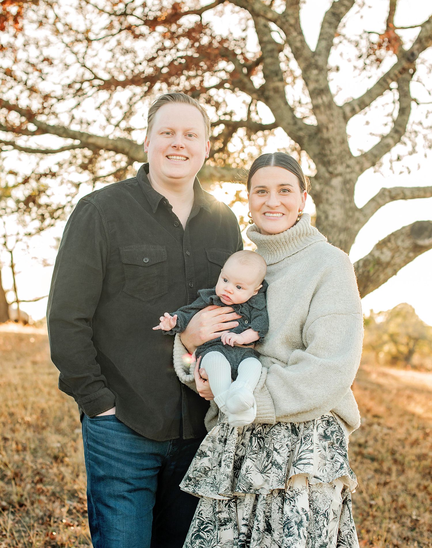 A family stands together outdoors against a backdrop of autumn trees during a golden sunset photoshoot in Fredericksburg, TX.