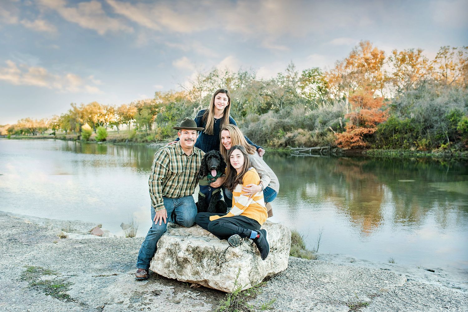 A series of outdoor family portrait photographs taken at sunset by a lake with autumn foliage in the background.