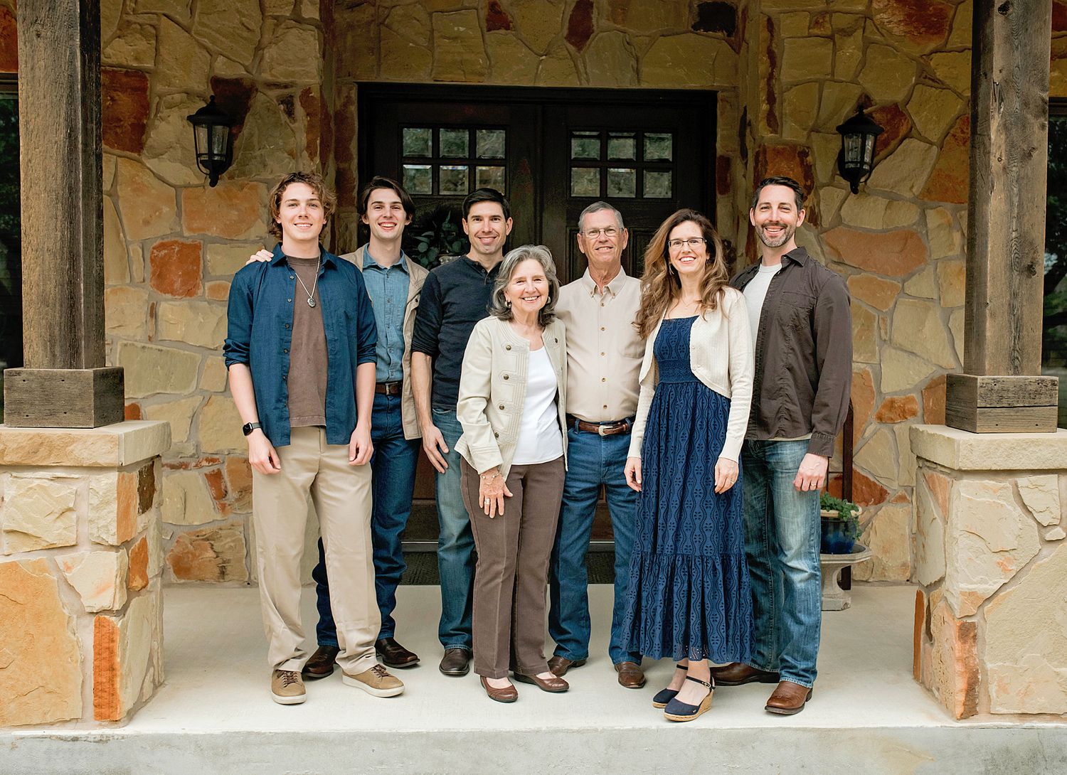 A happy family of seven poses together smiling in front of a rustic stone home entrance.