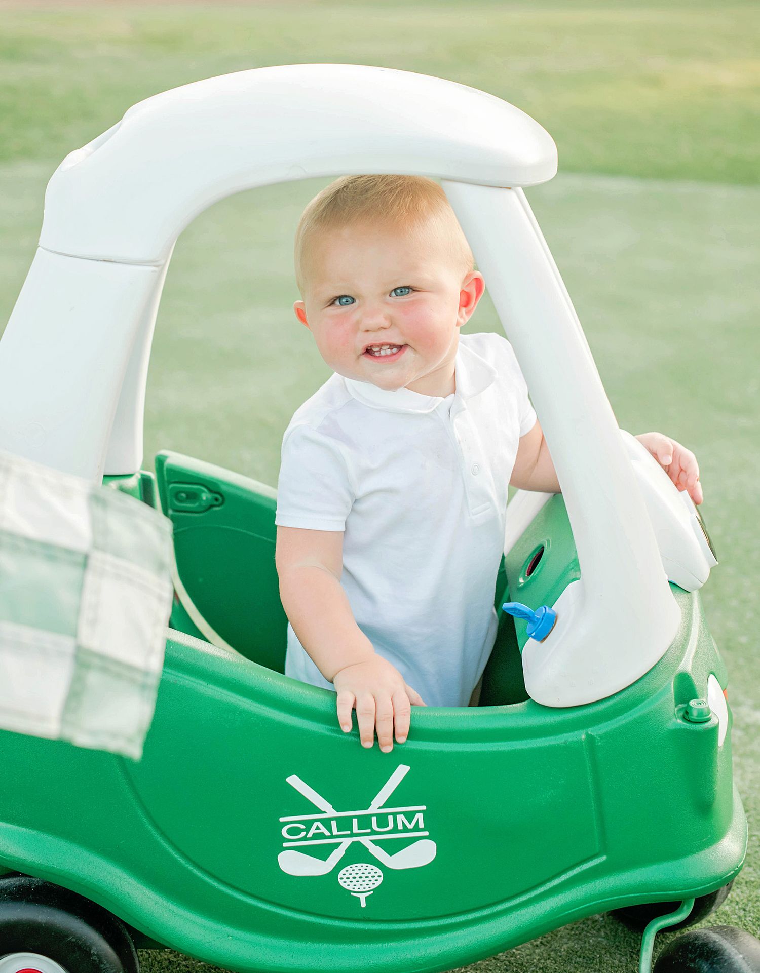 Small child riding in a green Little Tikes Cozy Coupe toy car in an outdoor setting.