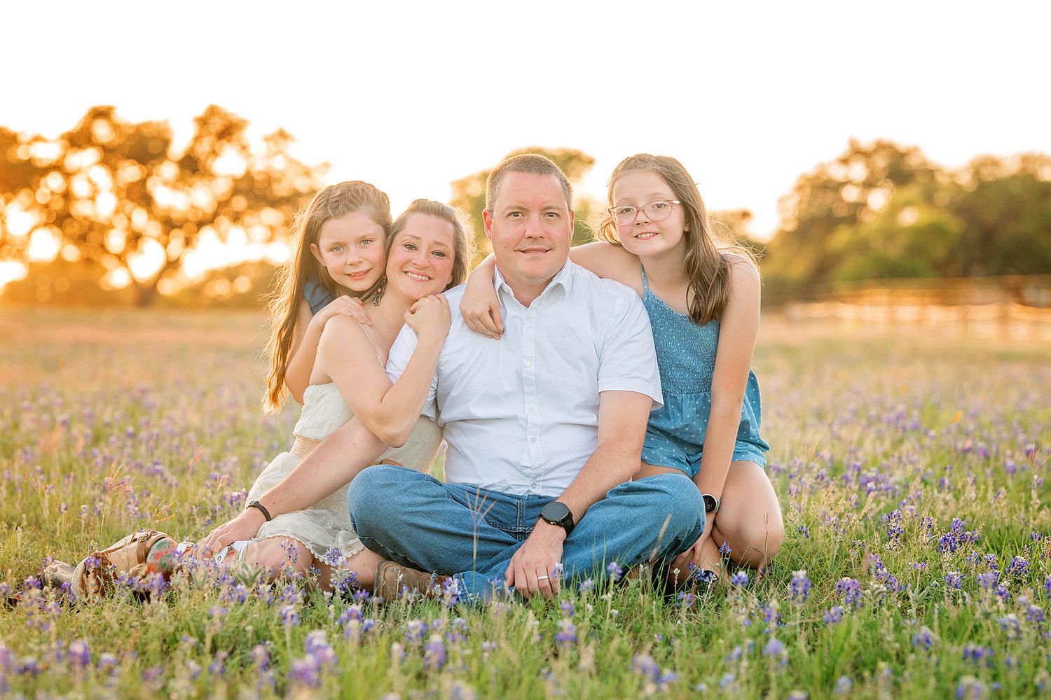 Family sits together in a field of bluebonnet during sunset with warm golden light. Blanco, TX