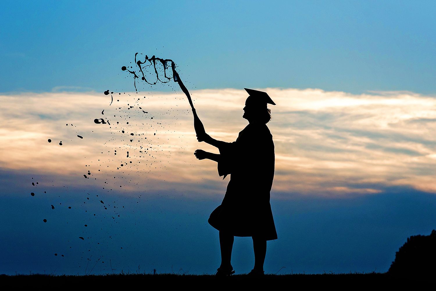 A graduate silhouetted against sunset sky pops champagne in celebration during graduation ceremony.