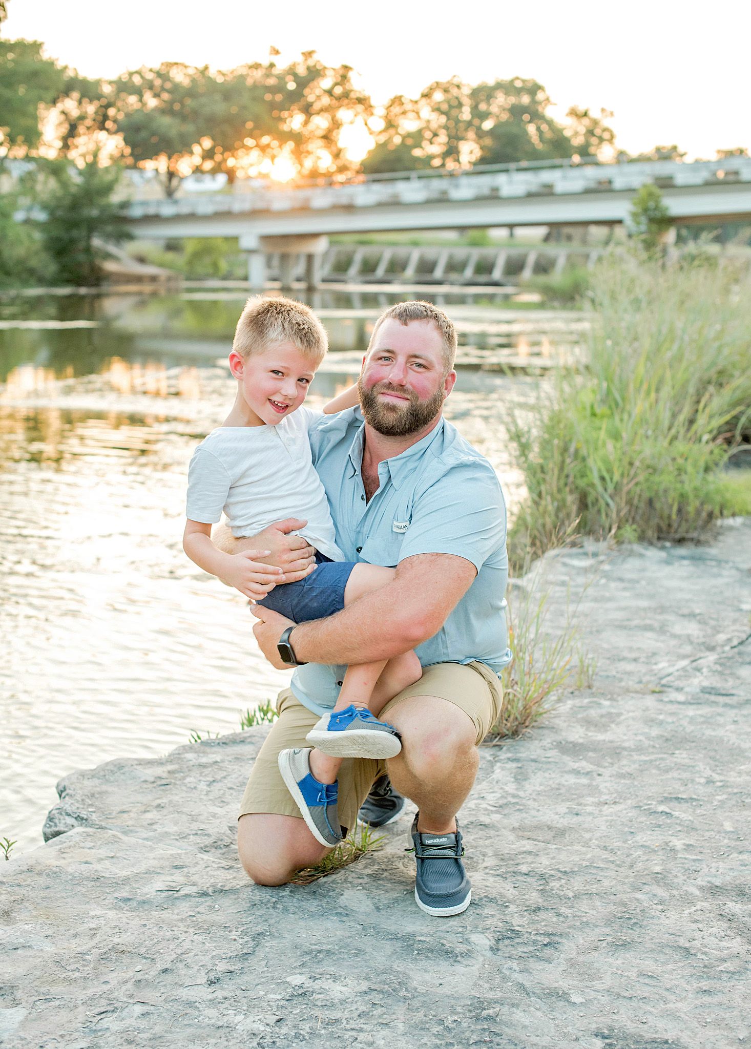 Parent and child share playful moments on a sandy beach at sunset near a tranquil lake.
