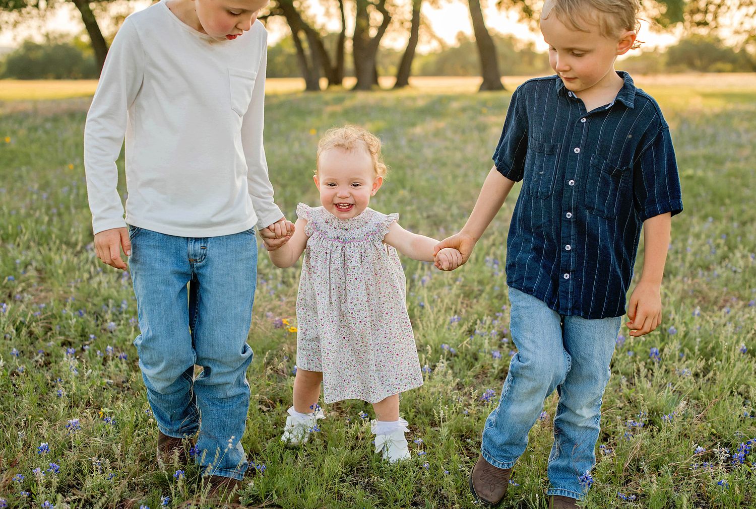 Three siblings walking together through a wildflower meadow at sunset.