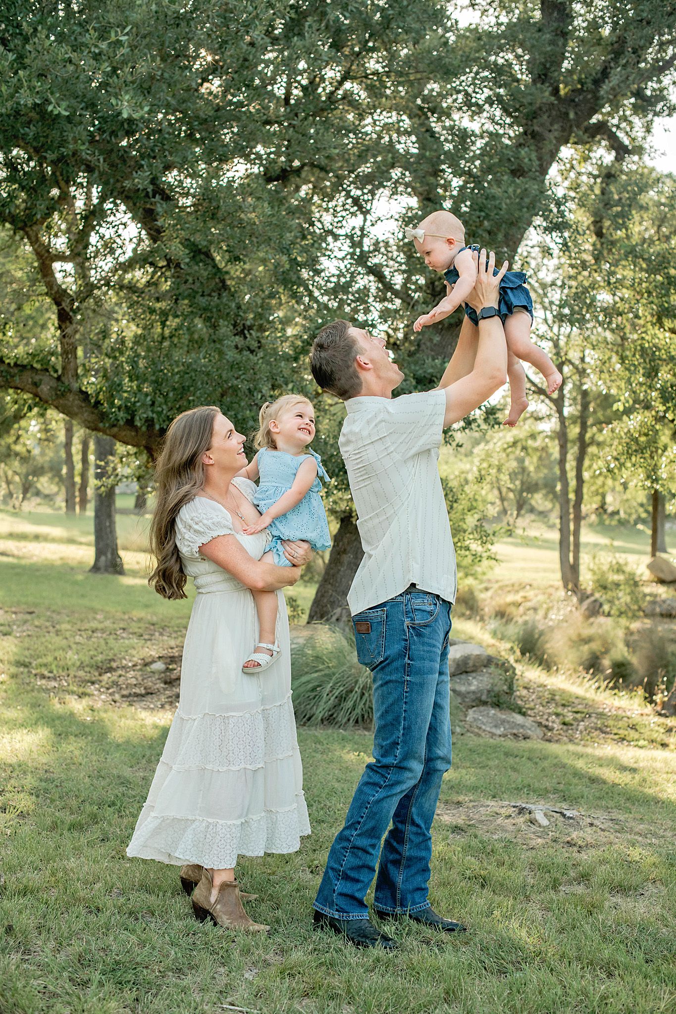 Happy family of four enjoying outdoor time, parents holding two young children in a lush green park setting.