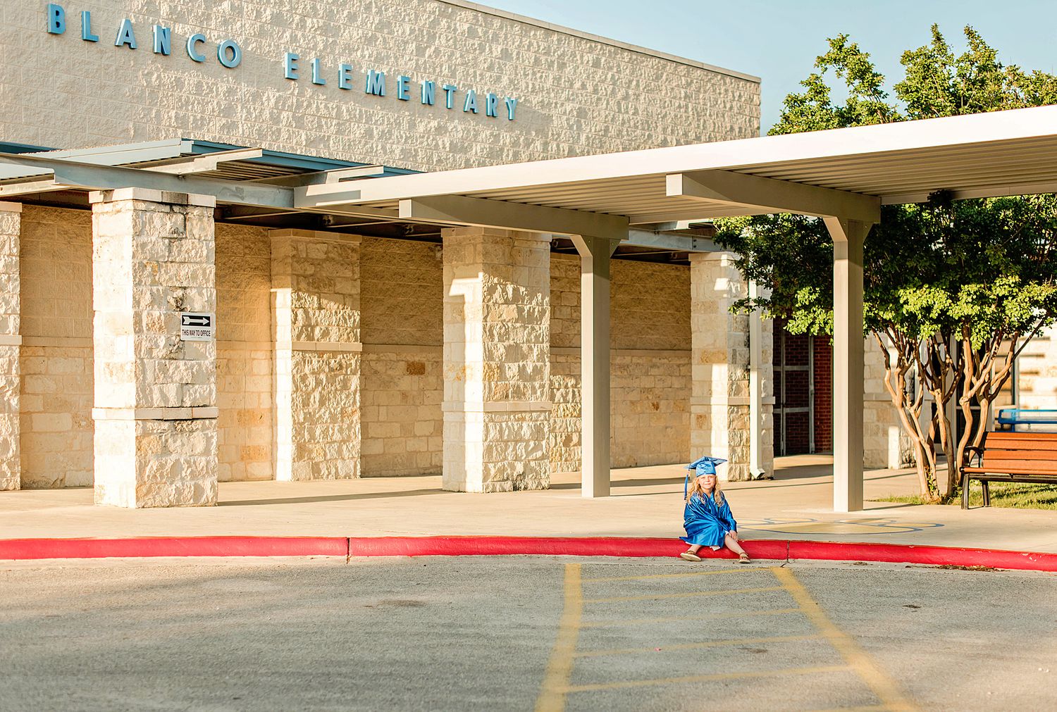 Kindergarten graduate site on the sidewalk in front of a elementary school building.