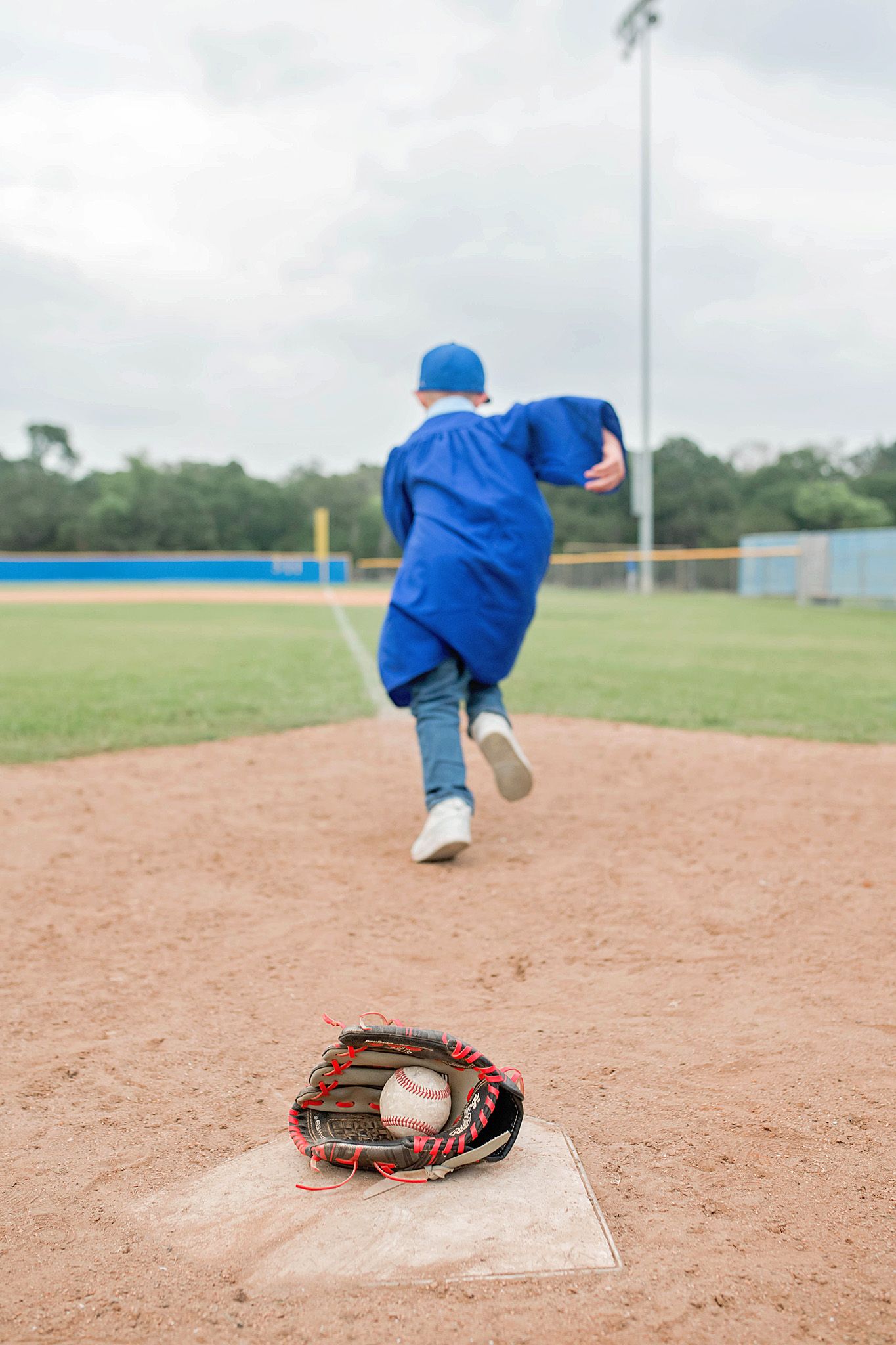 Young baseball player in blue uniform running from home plate with glove and ball on dirt field.