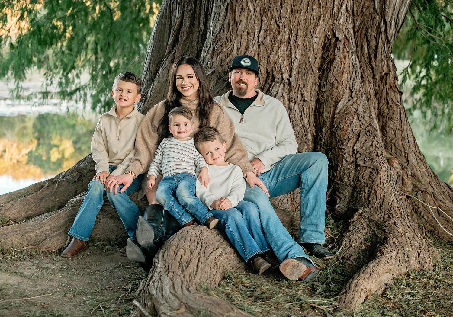 Family sitting together against a large tree trunk in a park during an outdoor photo session.
