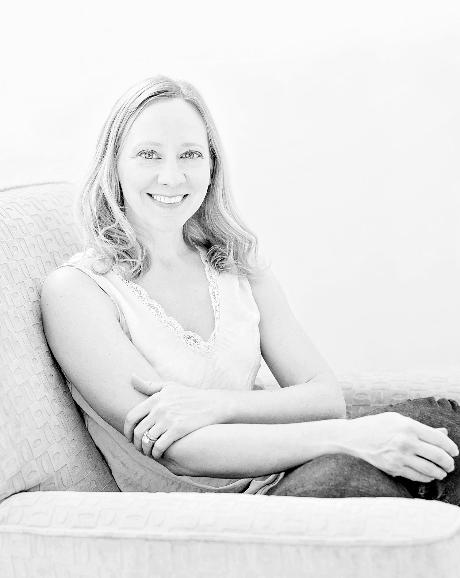 Black and white portrait photograph of a person smiling while relaxing on a couch in casual attire.