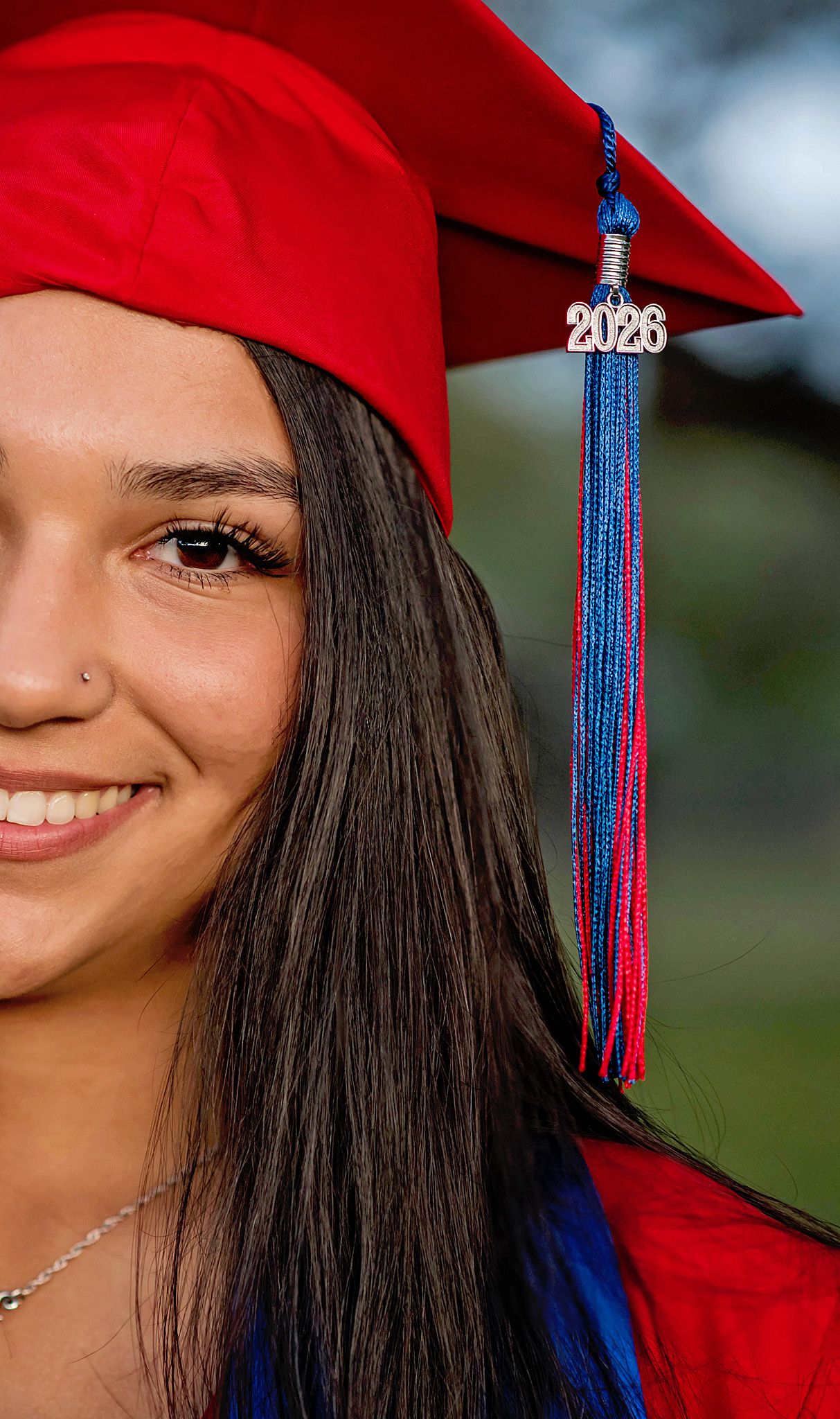 Smiling senior in red graduation cap and gown with blue and red tassel marked 2026.