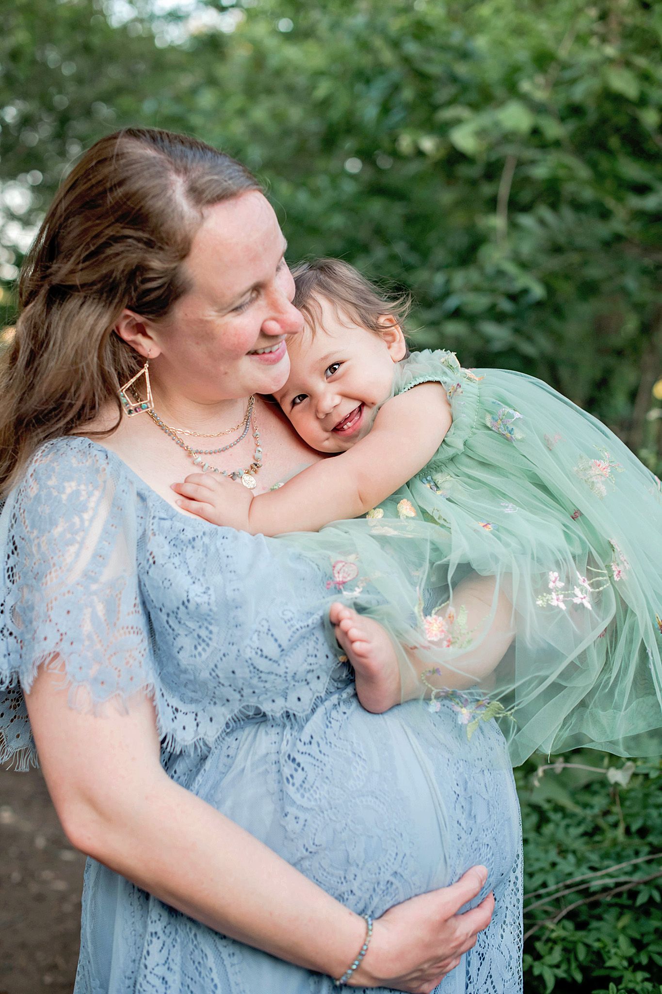 A couple in blue and mint green formal attire share an intimate embrace outdoors against a natural backdrop in Driftwood, TX.