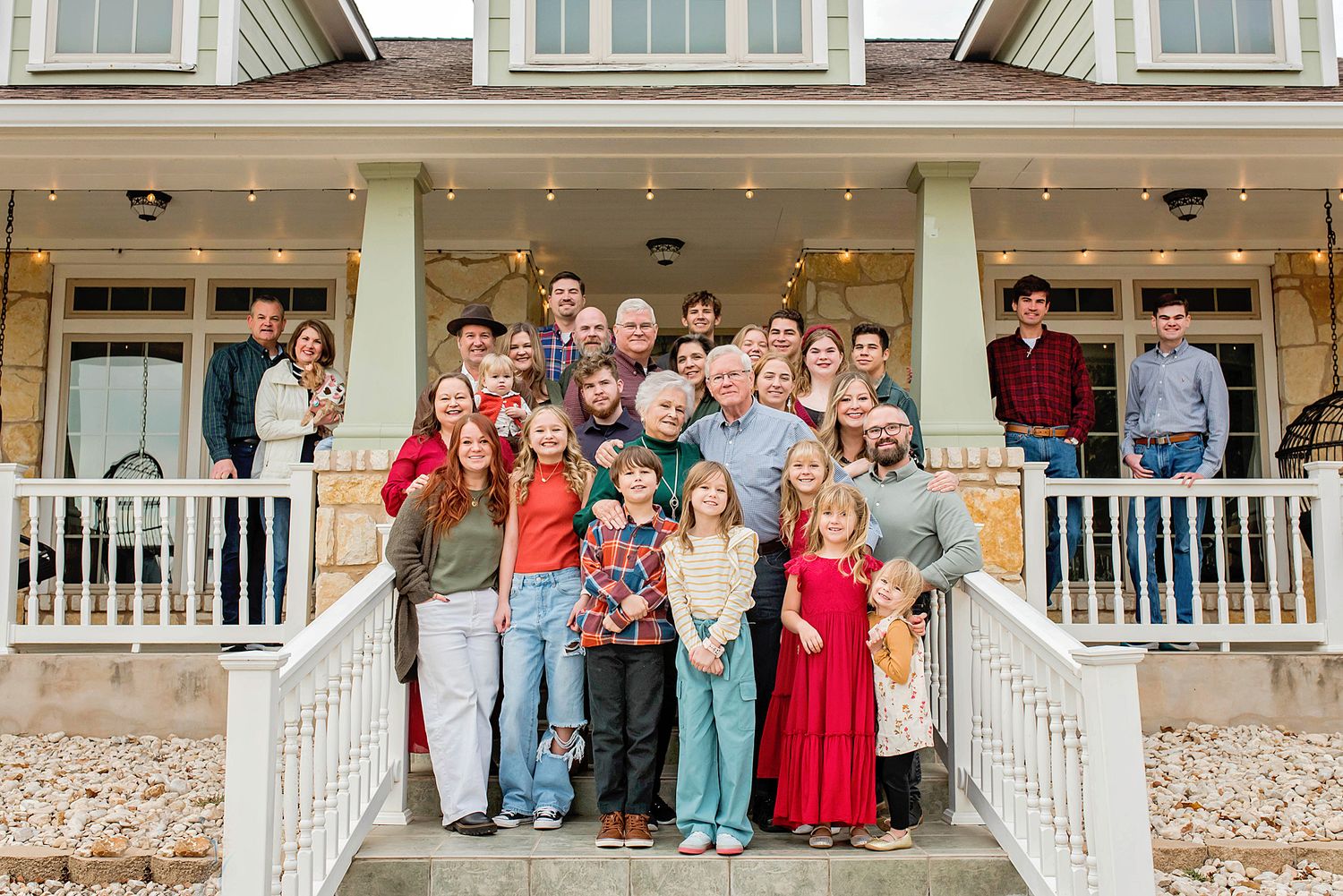Large multigenerational family posing together on the front porch steps of a beautiful two-story home.