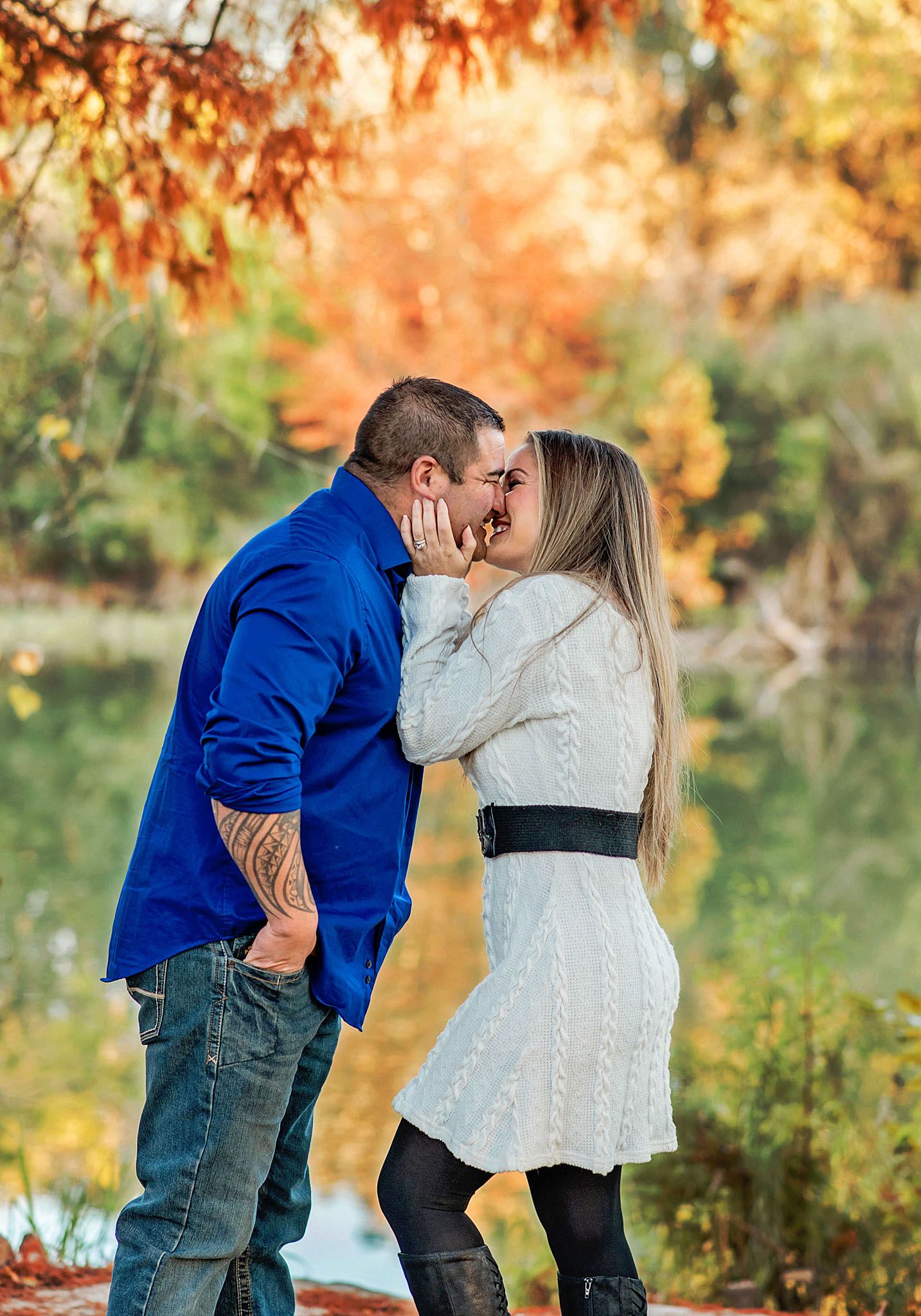 A couple shares a romantic kiss in an autumn setting with vibrant fall foliage in the background.