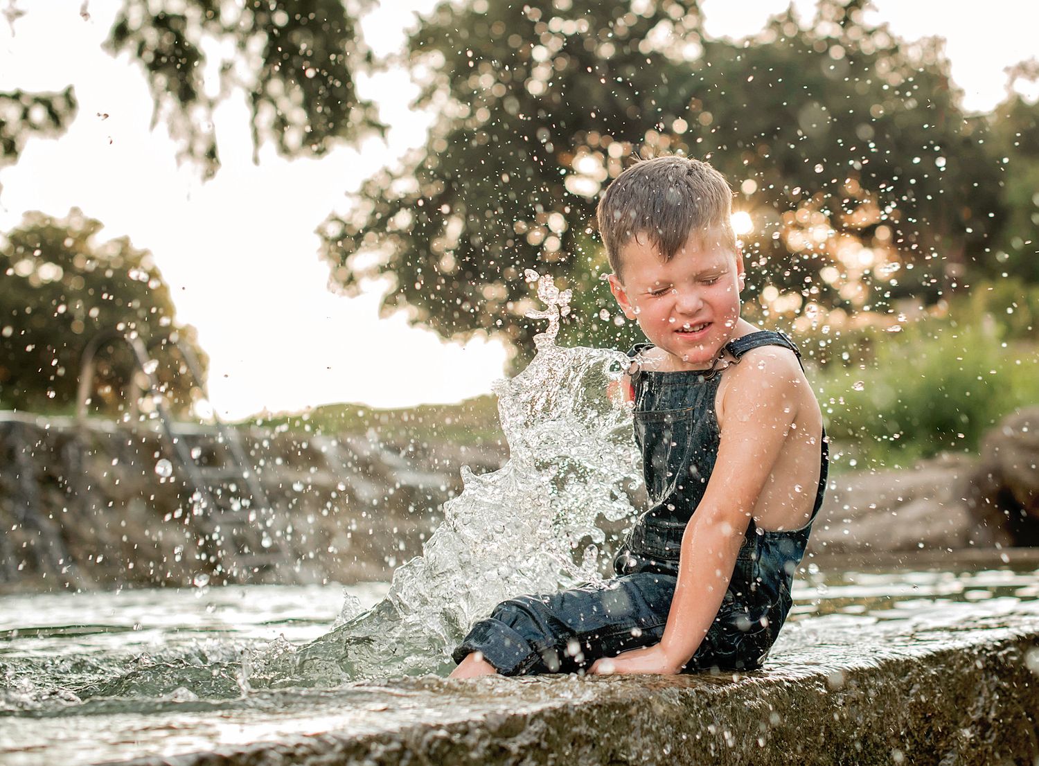 A person splashes joyfully in shallow water at sunset creating a dynamic spray of droplets against a golden sky.