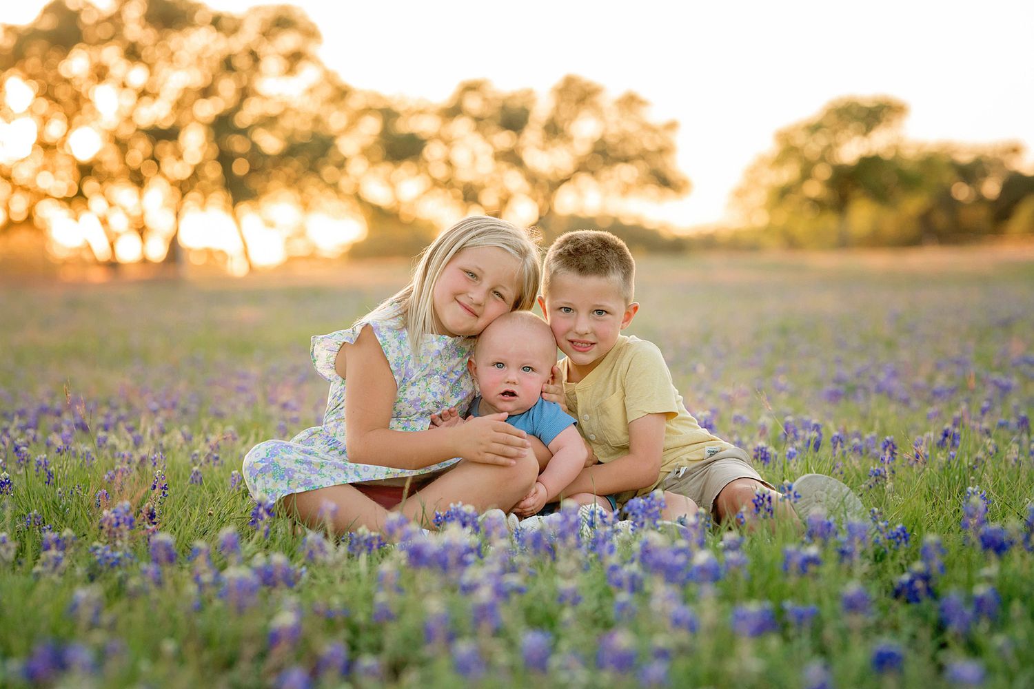 Children sitting together in a field of bluebonnets during golden hour.