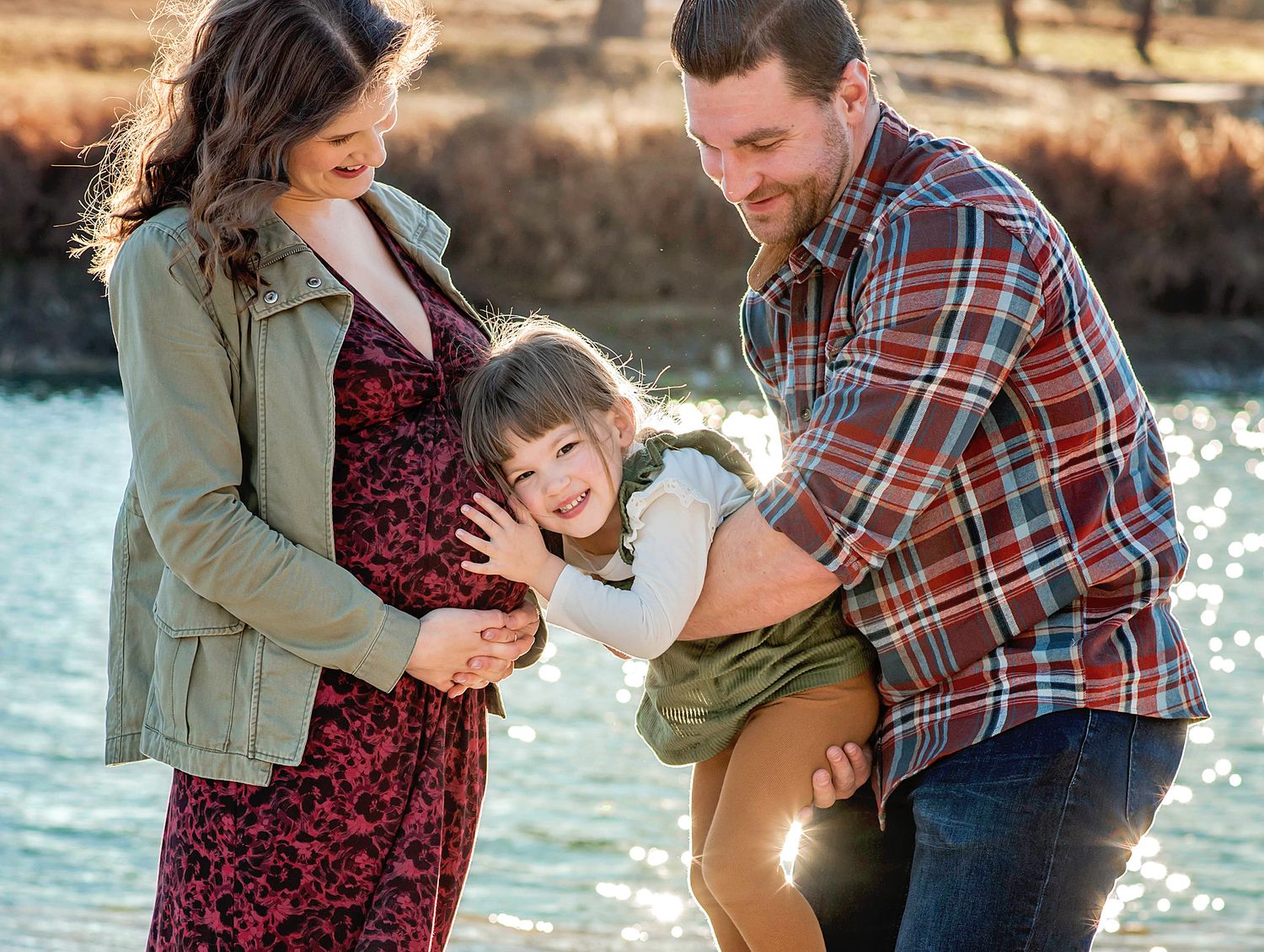 A family shares tender moments together by a sunlit lake on an autumn afternoon.
