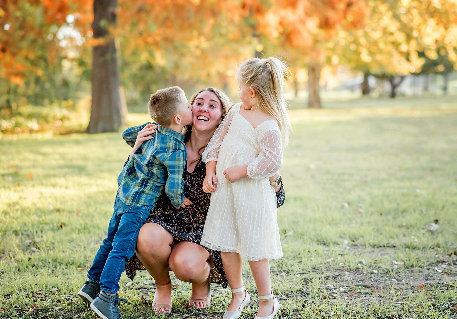 A family shares joyful moments together in a park during autumn with golden foliage in the background.