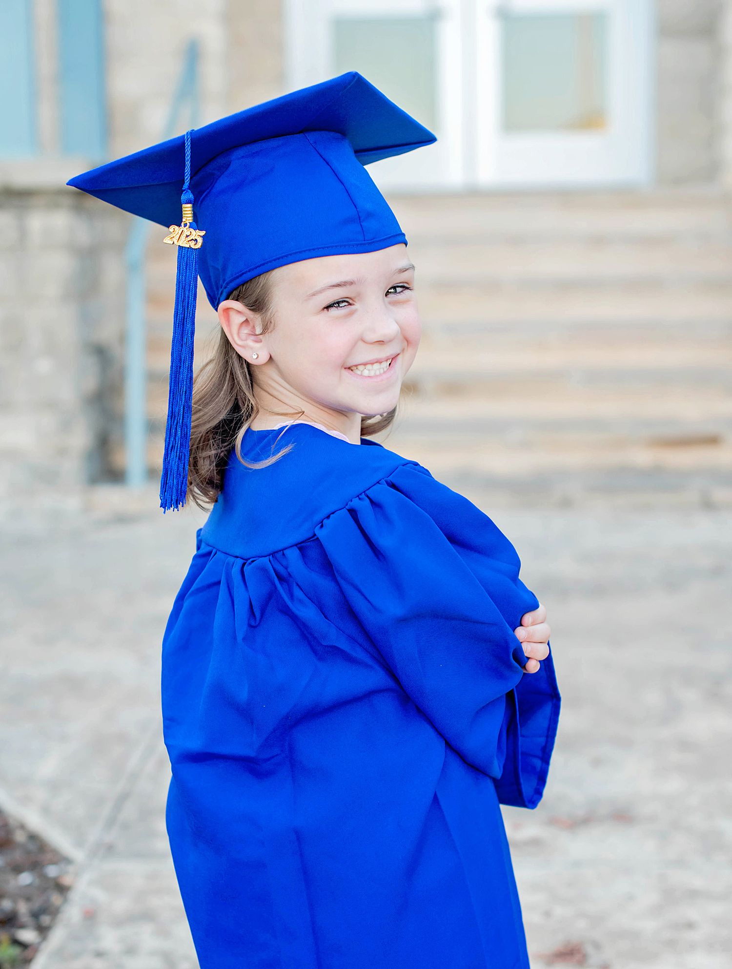 Graduate in bright blue cap and gown smiles joyfully during outdoor graduation photo session.