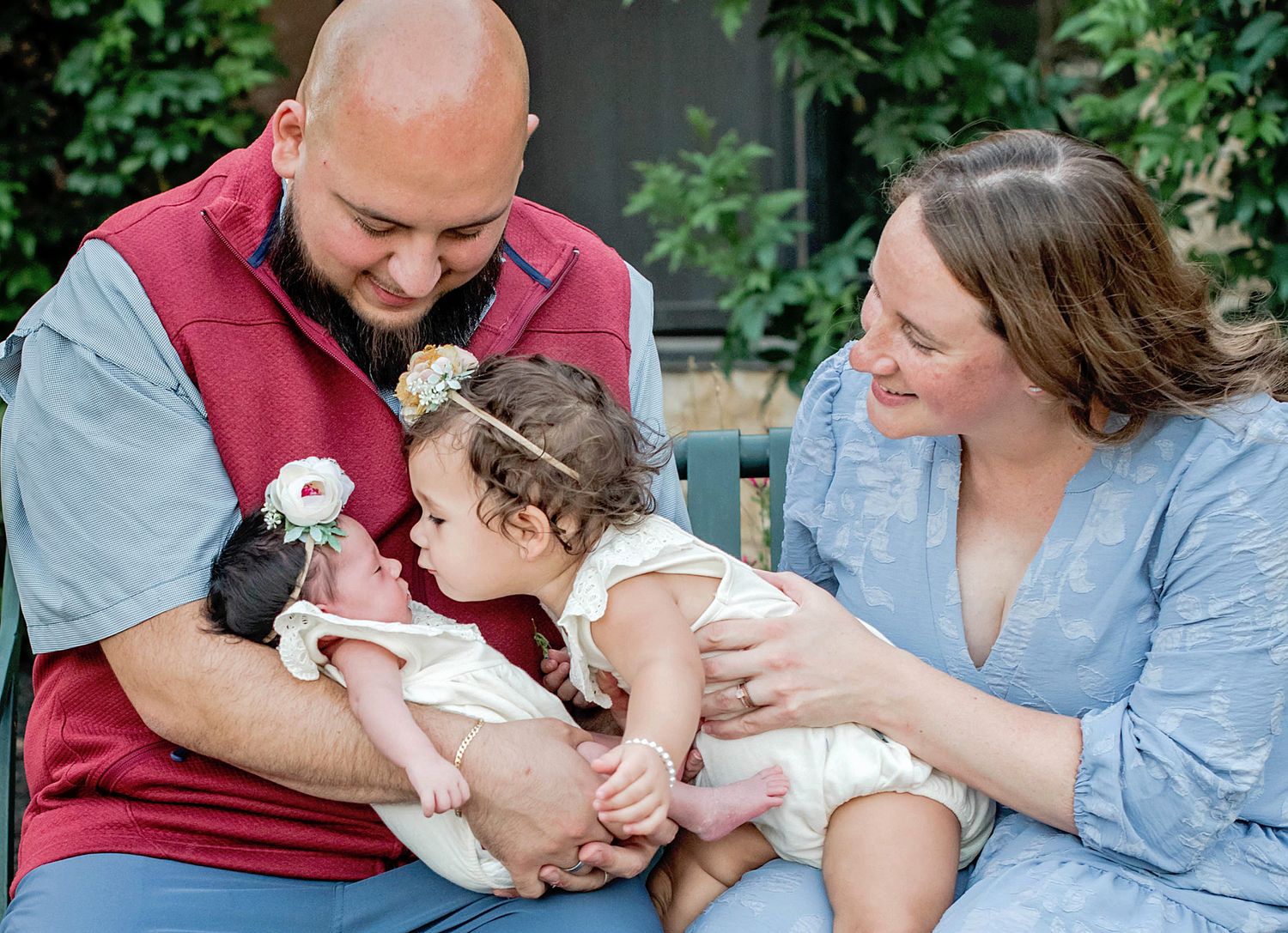 Family sitting outdoors together on bench sharing tender moment with newborn baby in casual attire in Buda, TX.