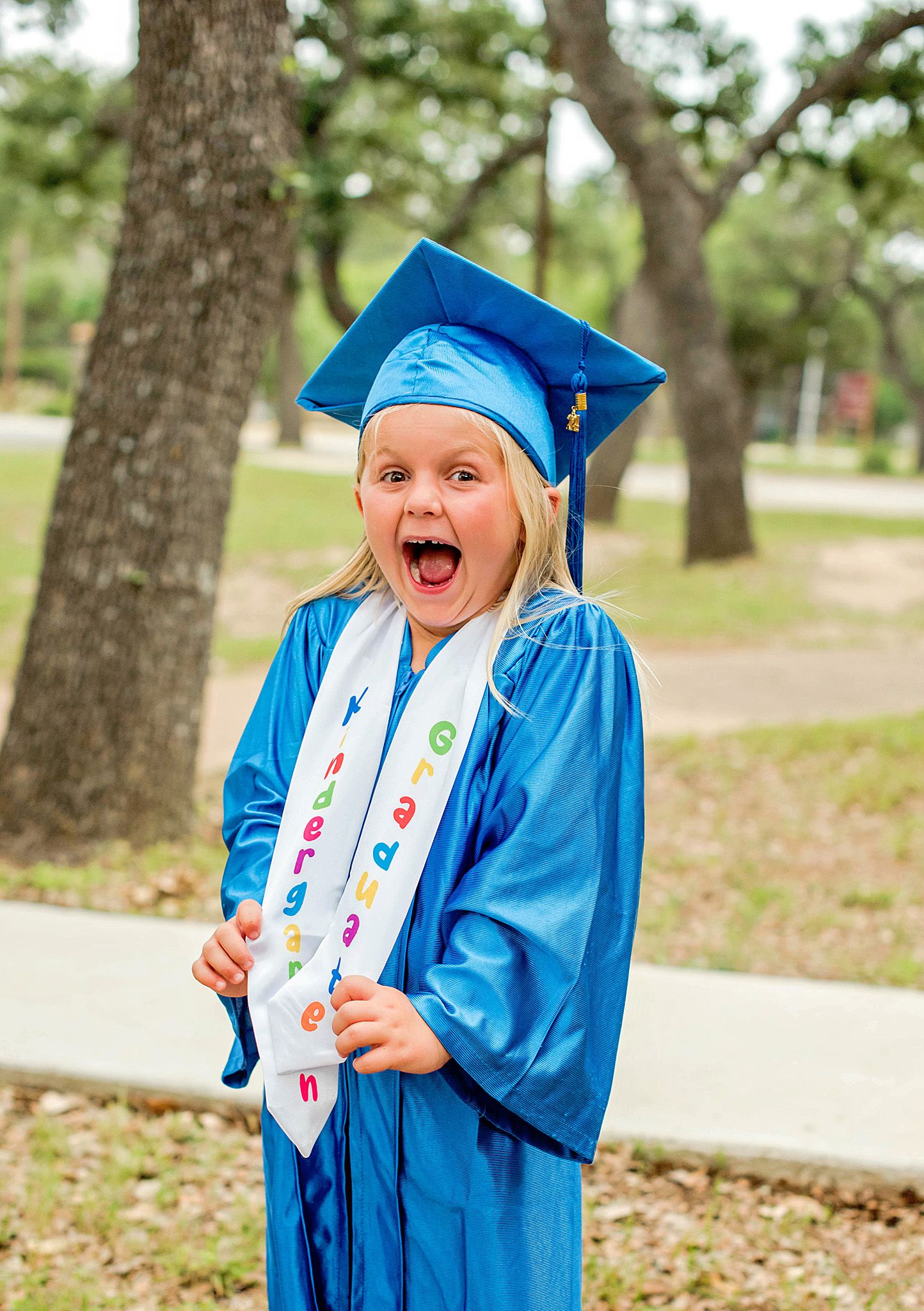 A graduate in bright blue cap and gown shows excitement during an outdoor photo session.