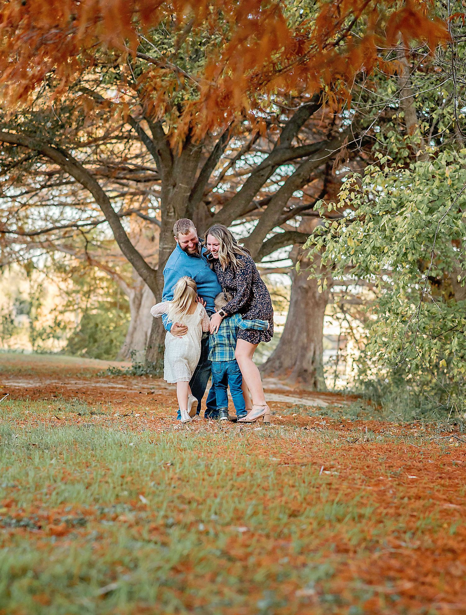 A family embraces during autumn under vibrant fall foliage in a scenic park setting.