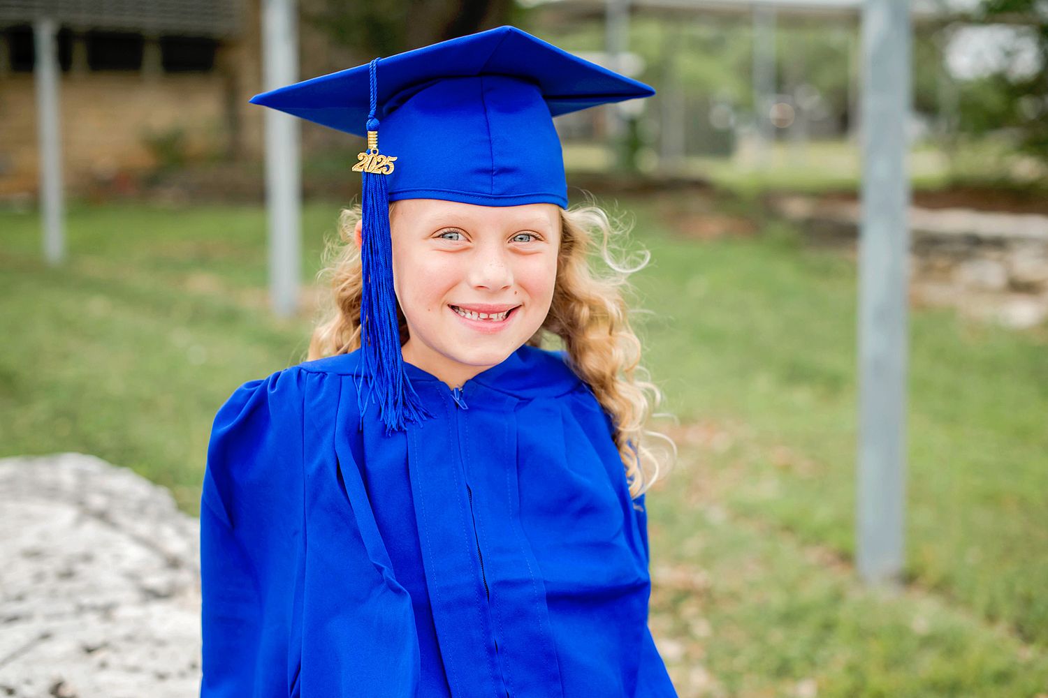 Graduate in bright blue cap and gown smiles joyfully during outdoor graduation photo session.
