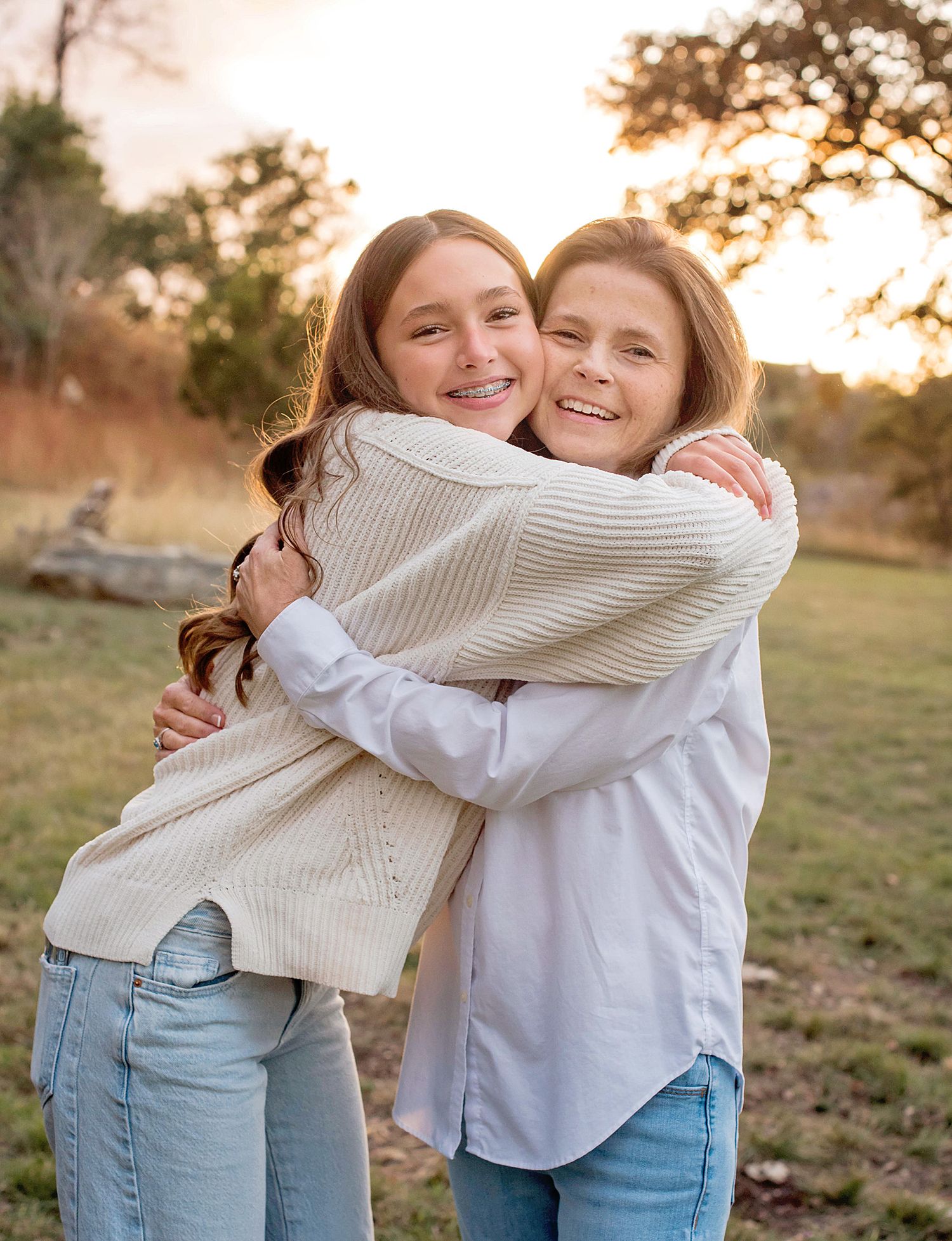 Two people sharing a warm embrace outdoors at sunset with autumn trees in the background.
