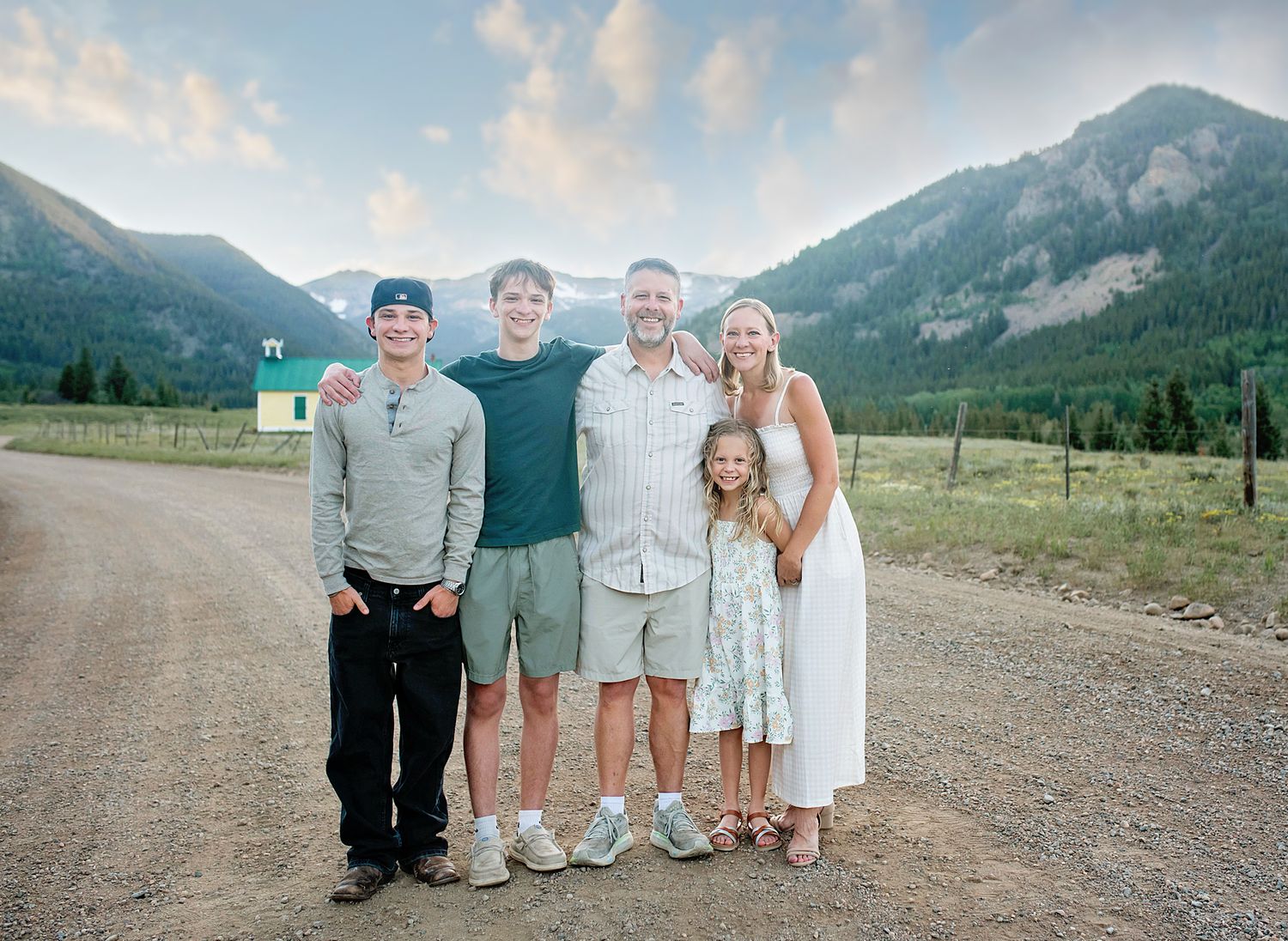 Family of five posing on a dirt road with scenic mountain landscape and green valleys in the background.